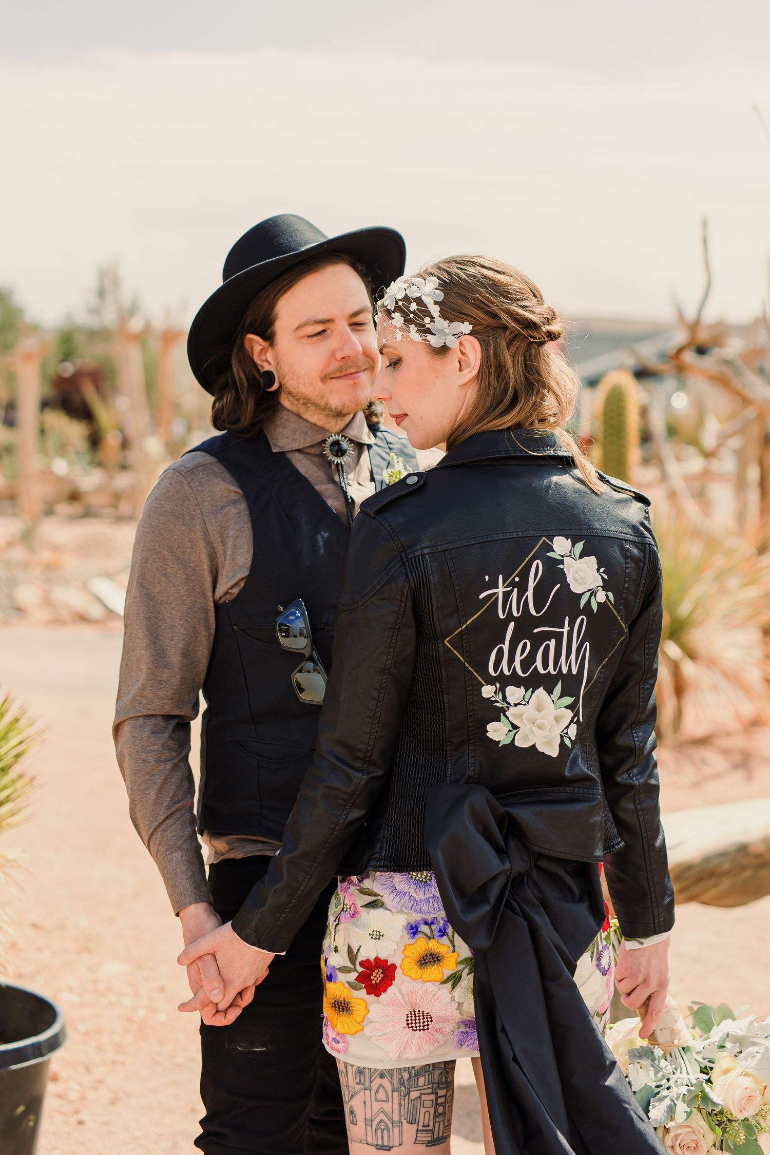 A couple wearing matching black jackets with custom text embraces in an outdoor desert setting.