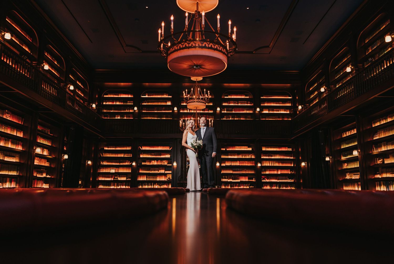 A luxurious library interior with dark wood shelving, warm lighting, and elegant chandeliers creating a dramatic ambiance.