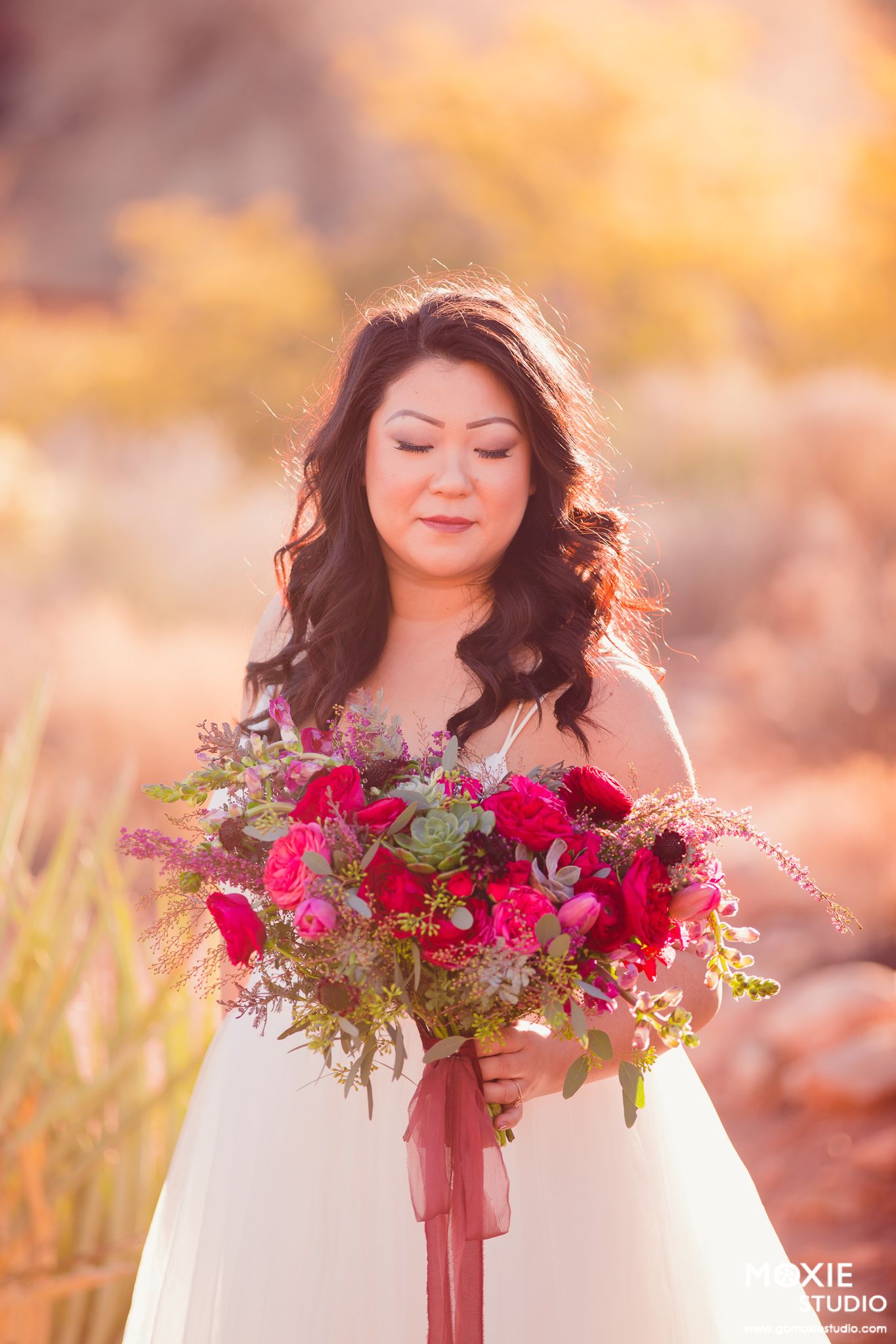 Woman in white dress holds vibrant red rose bouquet in dreamy autumn sunlit outdoor setting.