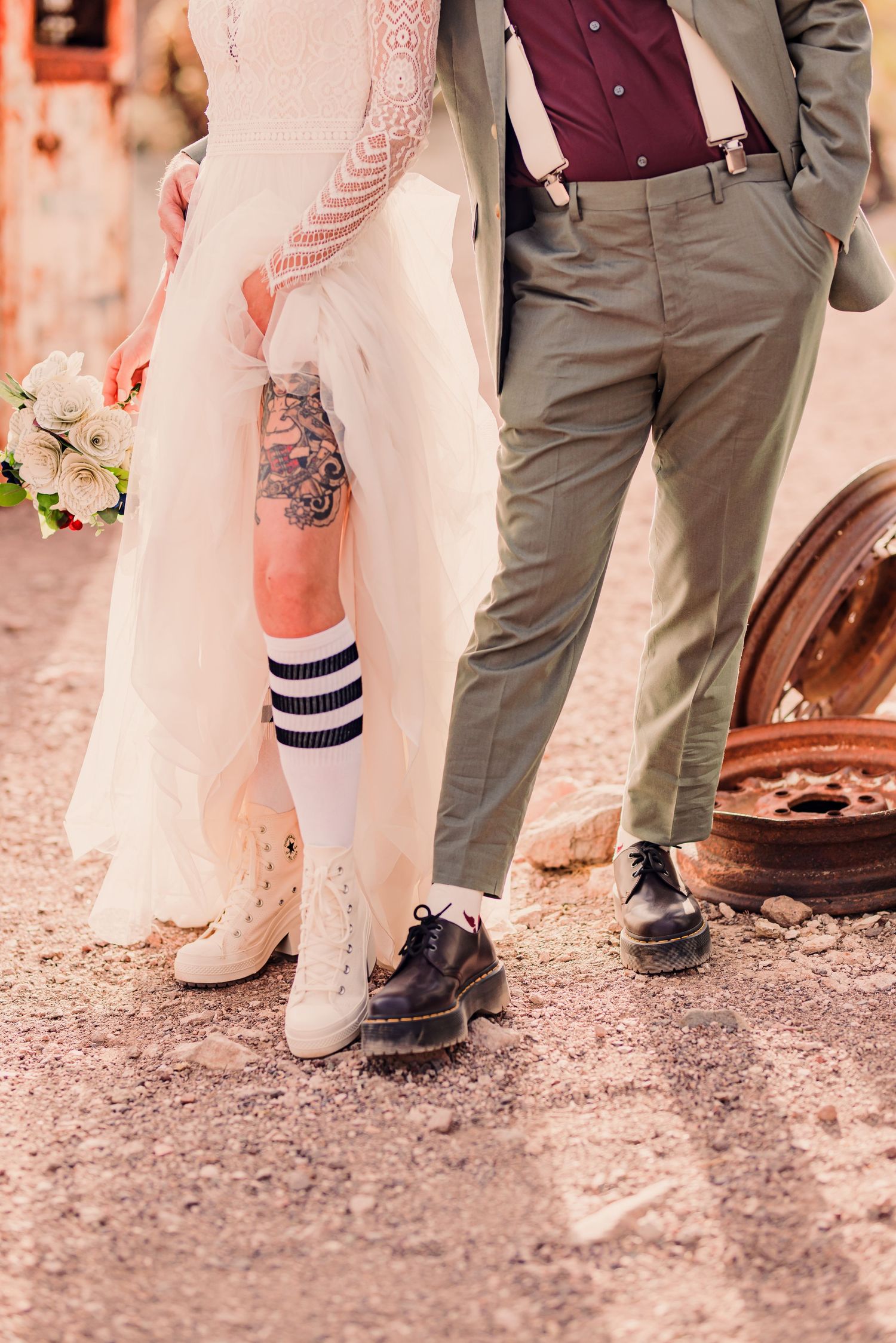 Wedding party shoes and dress hems shown from the knees down on rustic ground.