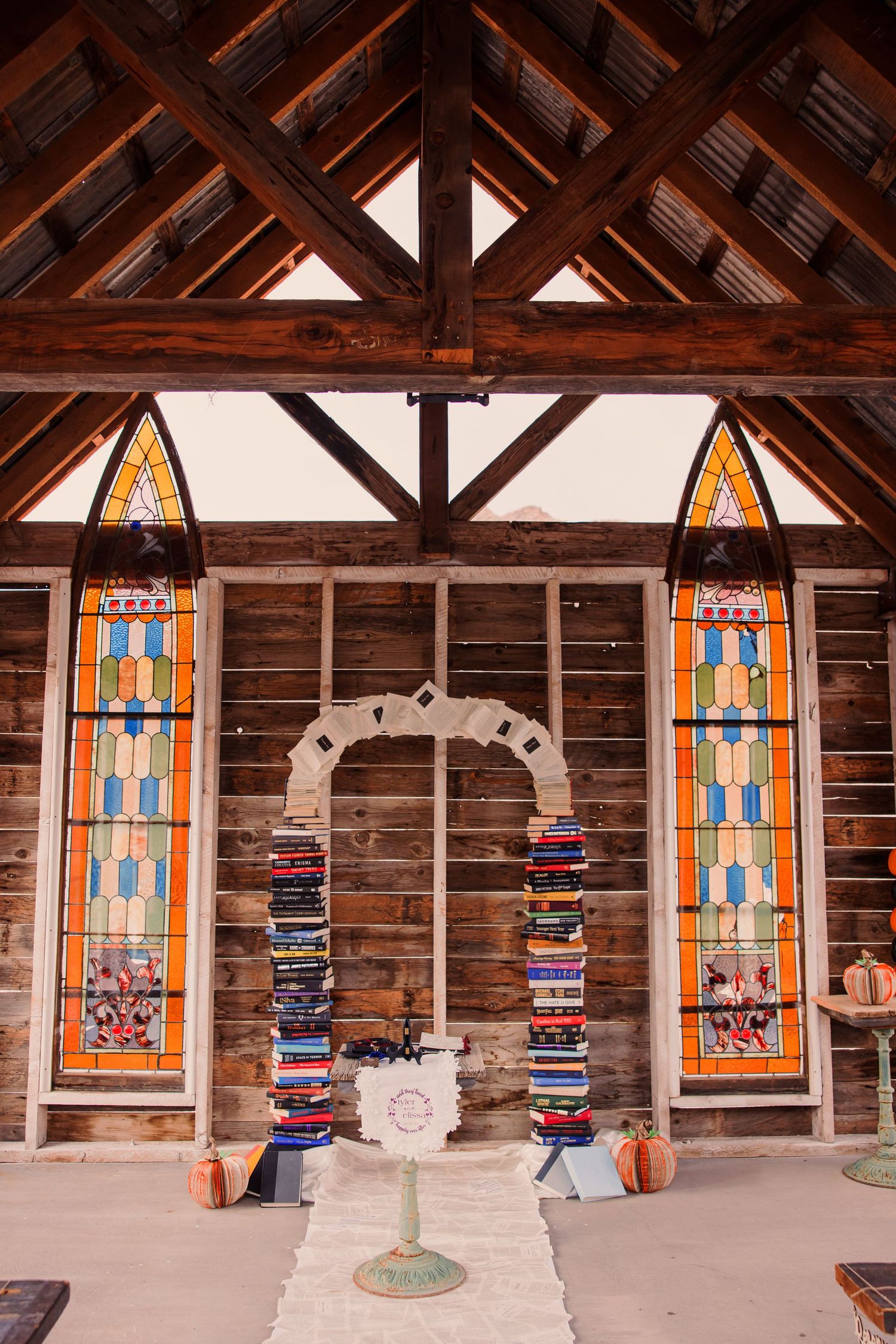 Rustic wooden chapel interior with two tall stained glass windows and decorative arch framing a birdbath centerpiece.