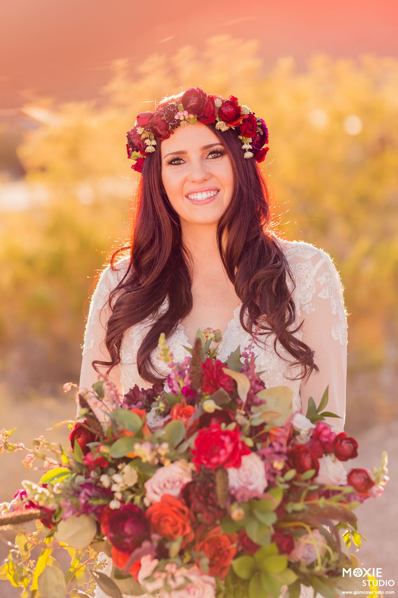 A romantic sunset photoshoot features a floral crown and deep red bouquet with roses and greenery.