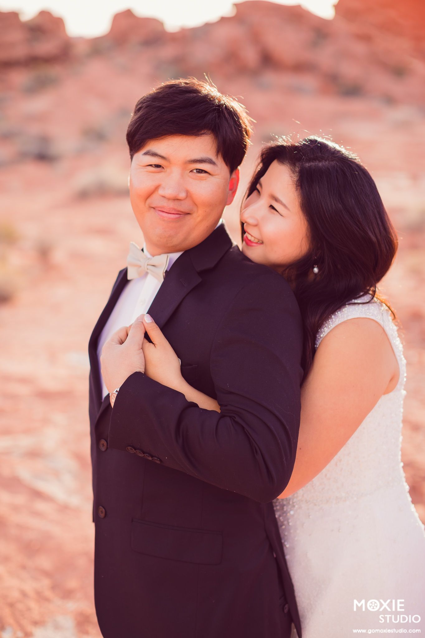 A romantic couple shares tender moments against a warm sunset backdrop at a desert location.