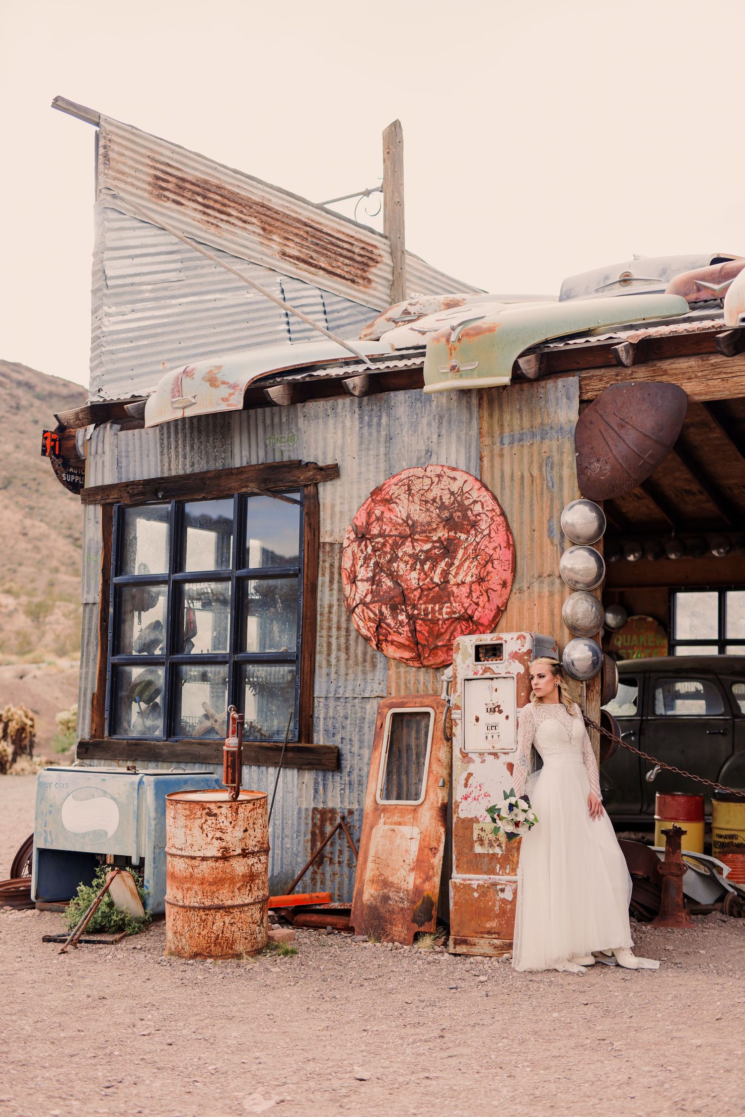 Rustic desert building exterior with vintage metal decorations and white dress display against weathered walls.