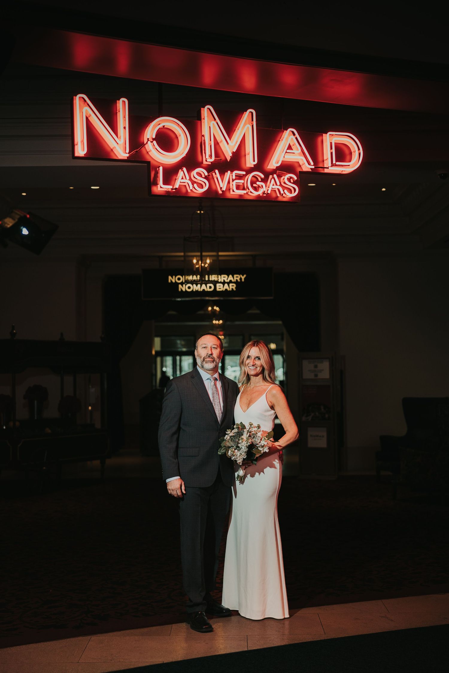 A couple poses together at night under illuminated red neon signs at the Nomad Las Vegas hotel.