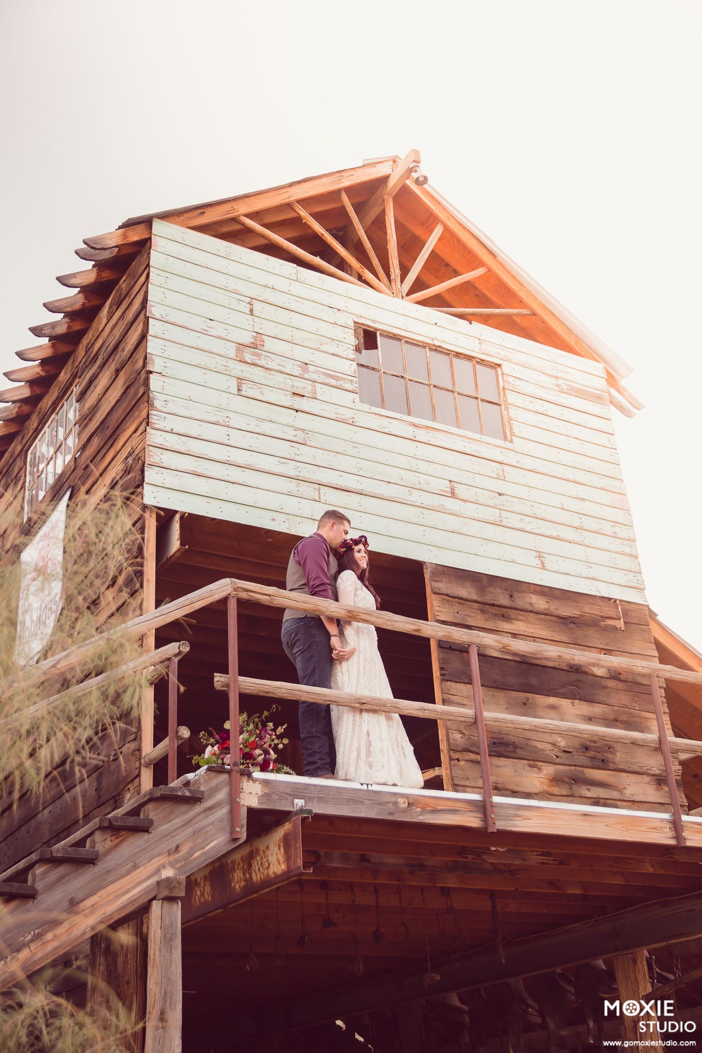 A romantic couple shares a kiss on a rustic wooden deck with sunlight streaming through the slats above.