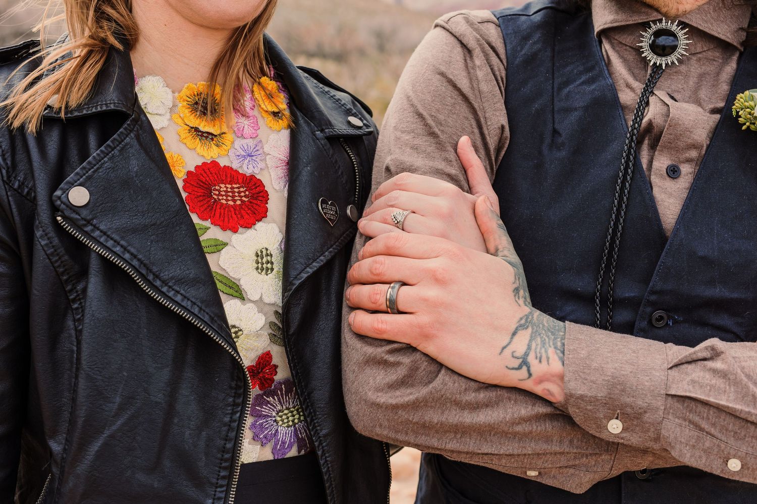 A couple wearing casual outerwear embraces while standing outdoors in an autumn setting.