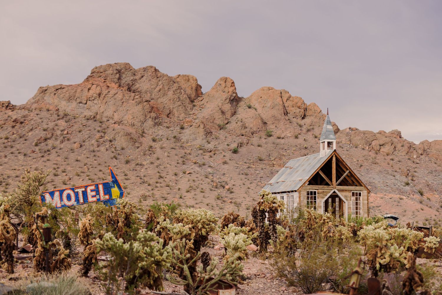 A panoramic view of desert motel buildings and rustic structures nestled among rocky mountains in a remote landscape.