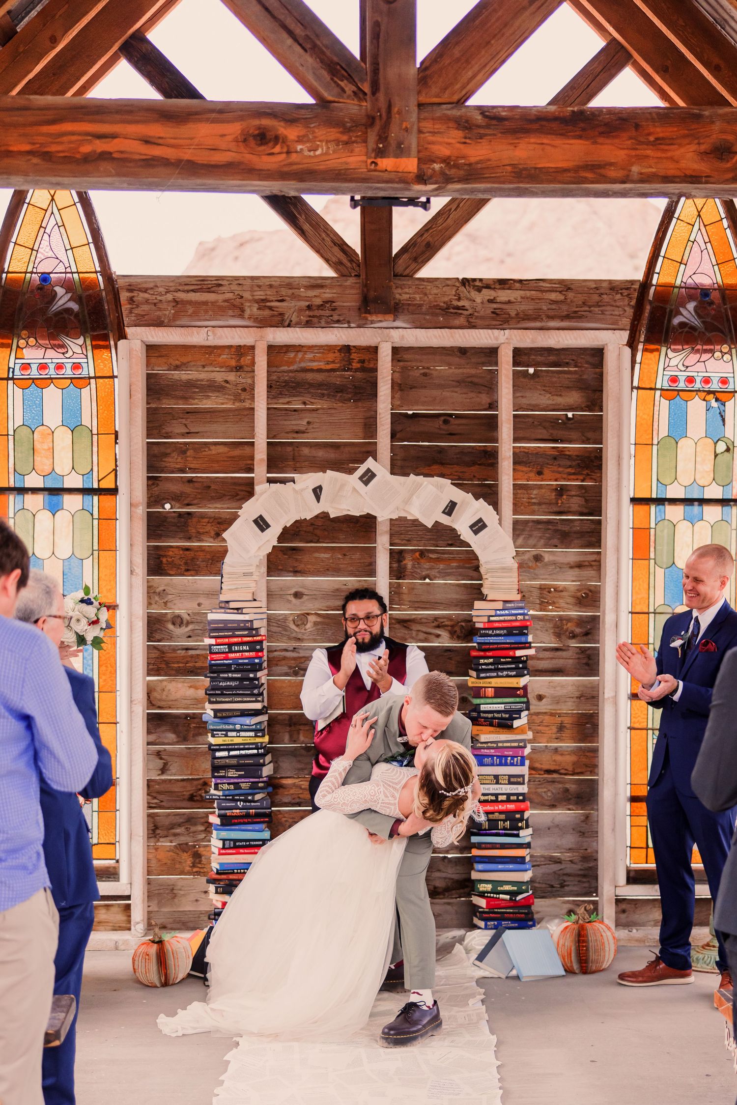 A rustic wedding ceremony setup with stained glass windows and stacks of books creating an archway at an indoor venue.