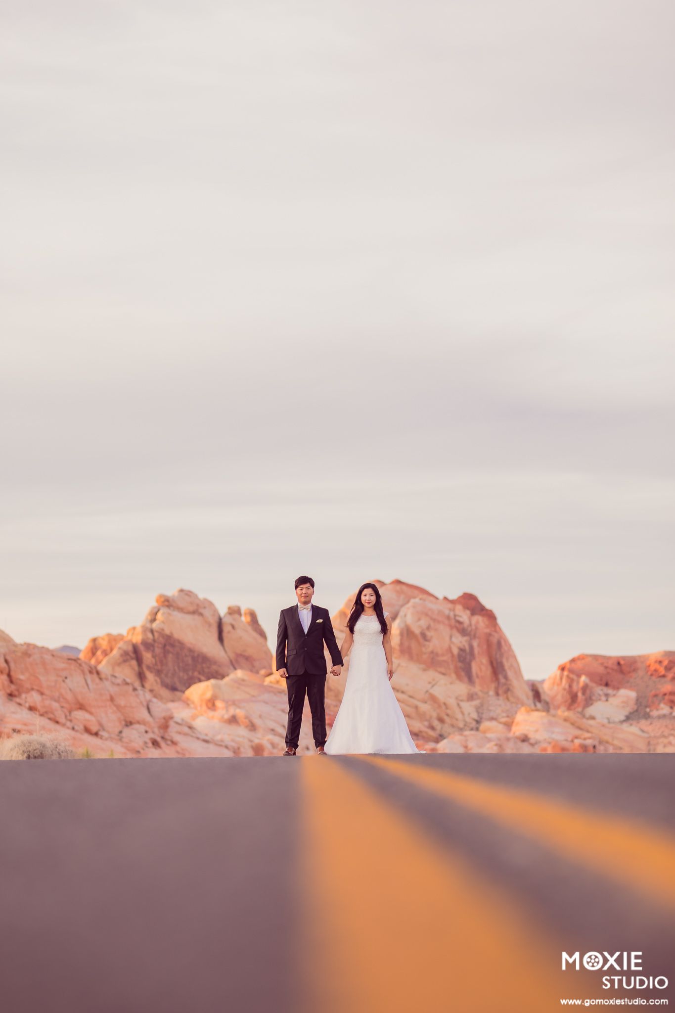 A couple poses against dramatic red rock formations at Valley of Fire during golden hour sunset.