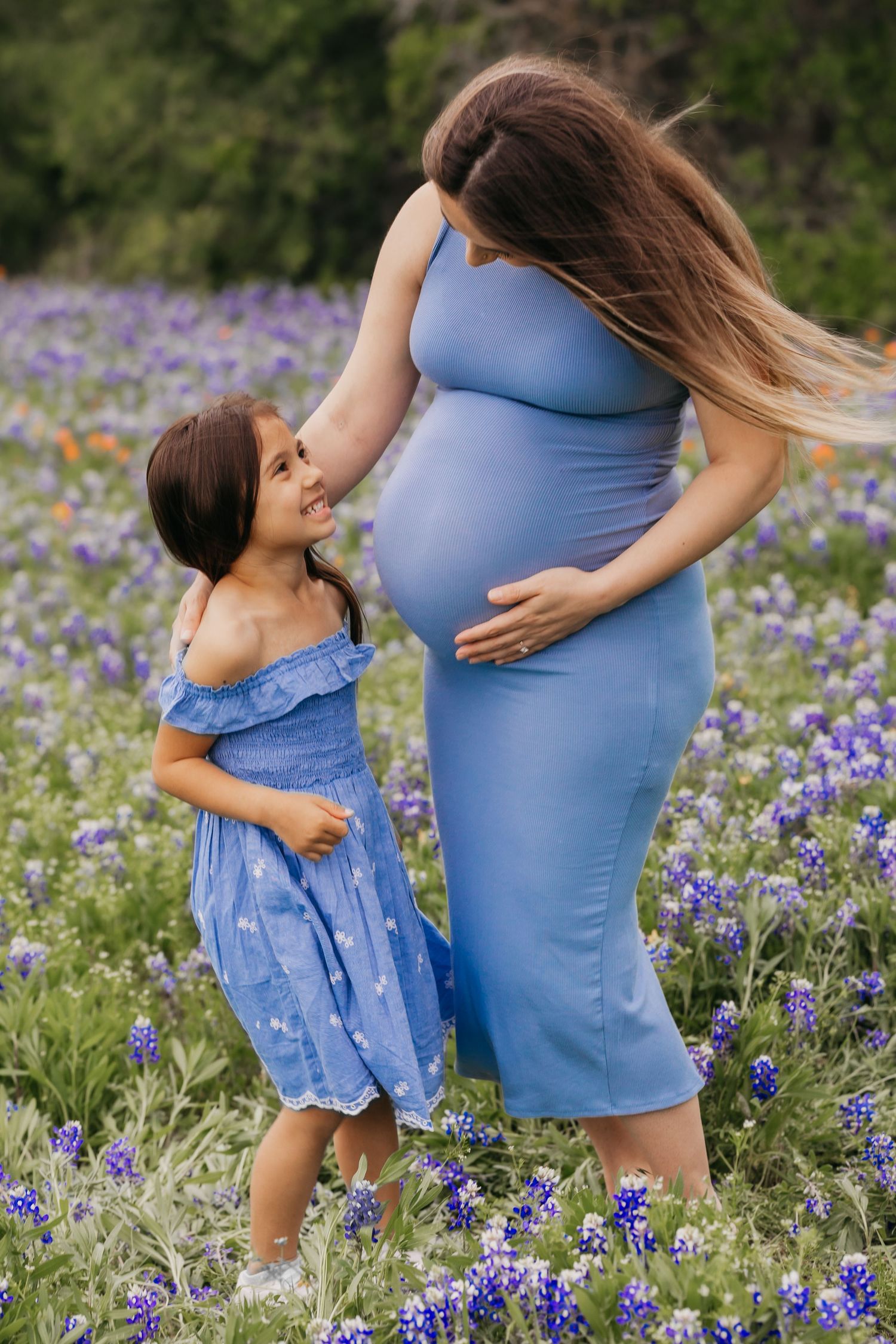 Pregnant woman in a flowy dress posing in a vibrant field of bluebonnets in Central Texas during a maternity photo session