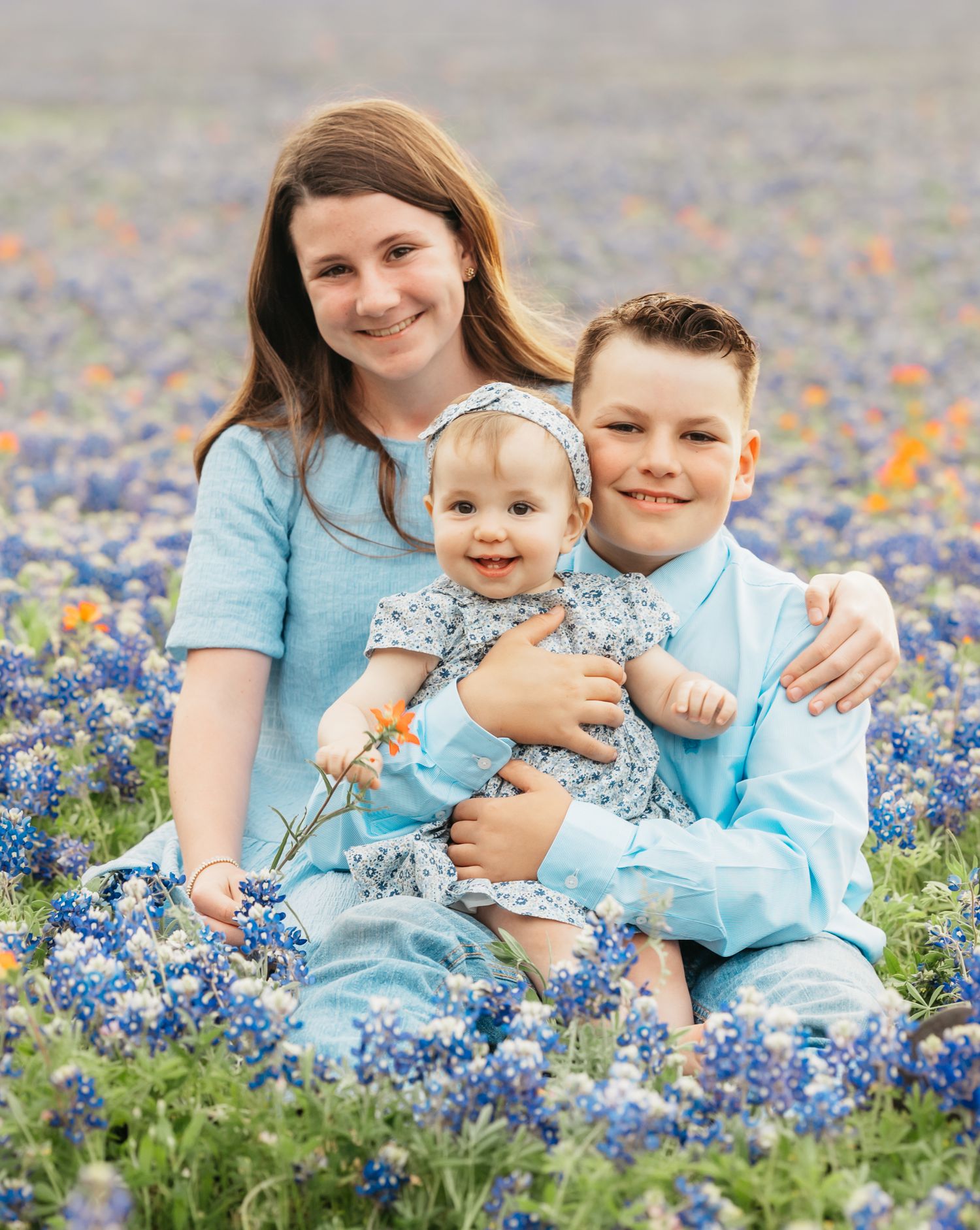 Three kids sitting together in a field of blooming bluebonnets in Georgetown, Texas, enjoying a sunny spring day