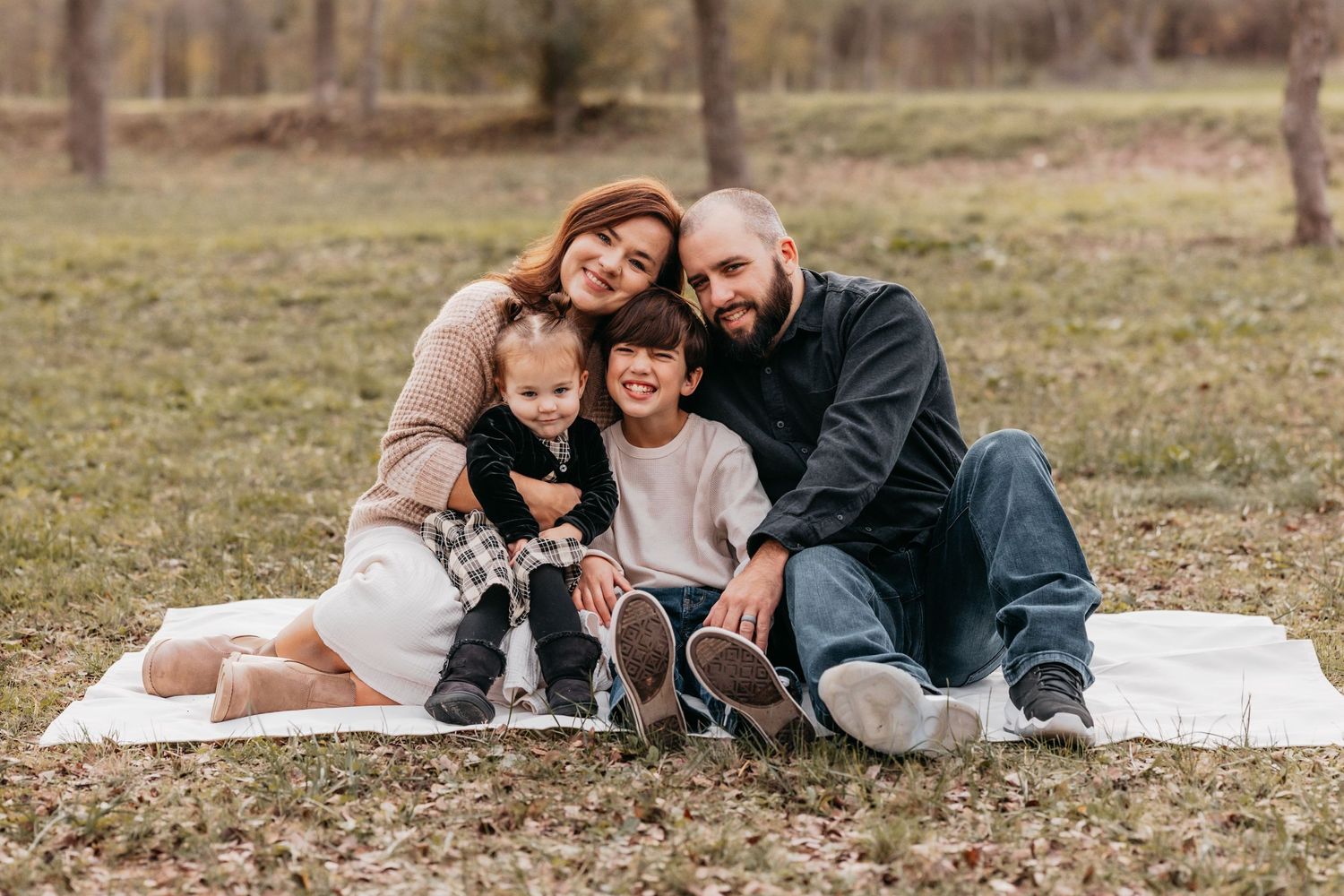 Family of four sitting together among vibrant fall leaves during an outdoor autumn photo session in Belton, Texas