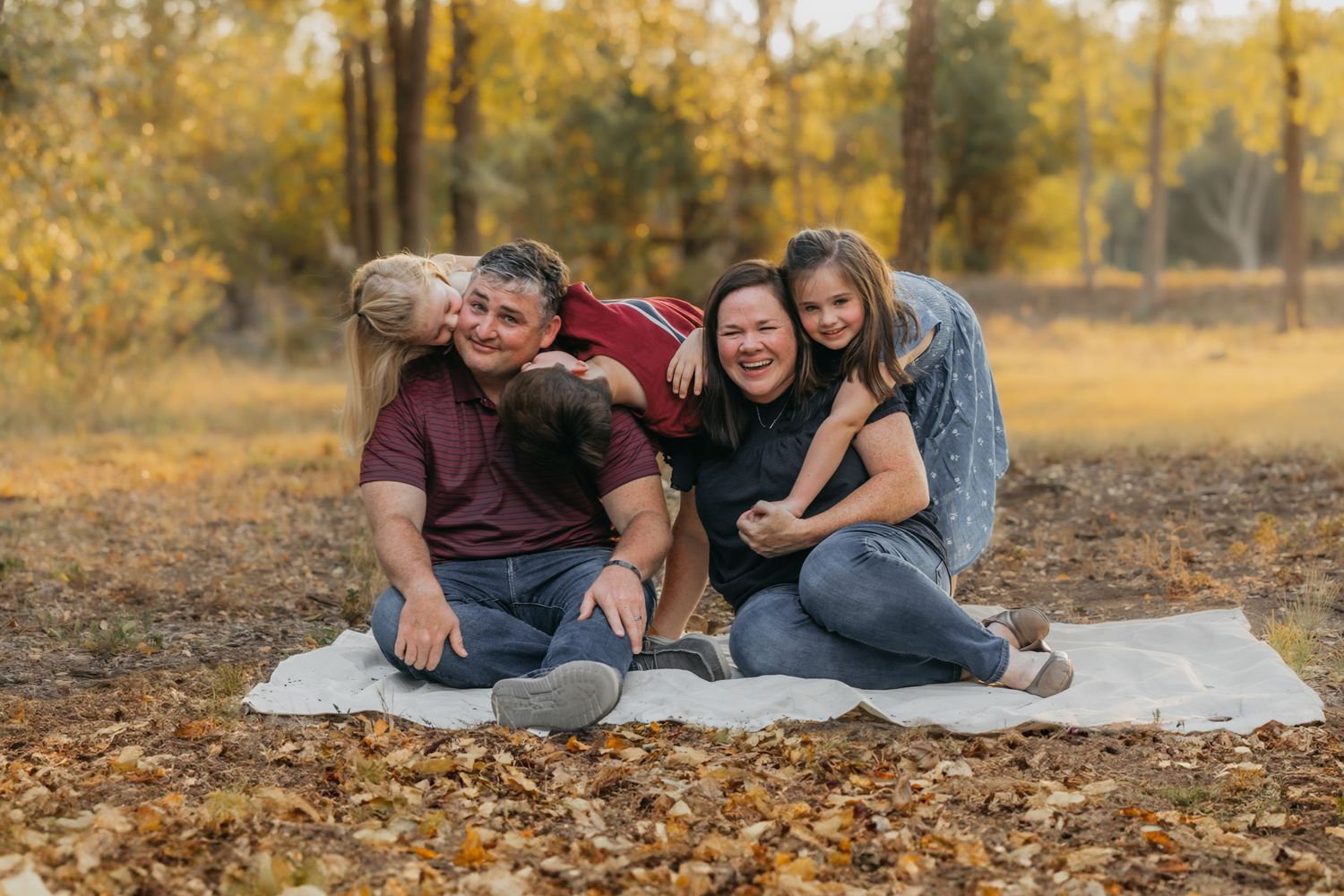 Mom, dad, and three kids smiling together while sitting among colorful fall leaves during a family photo session