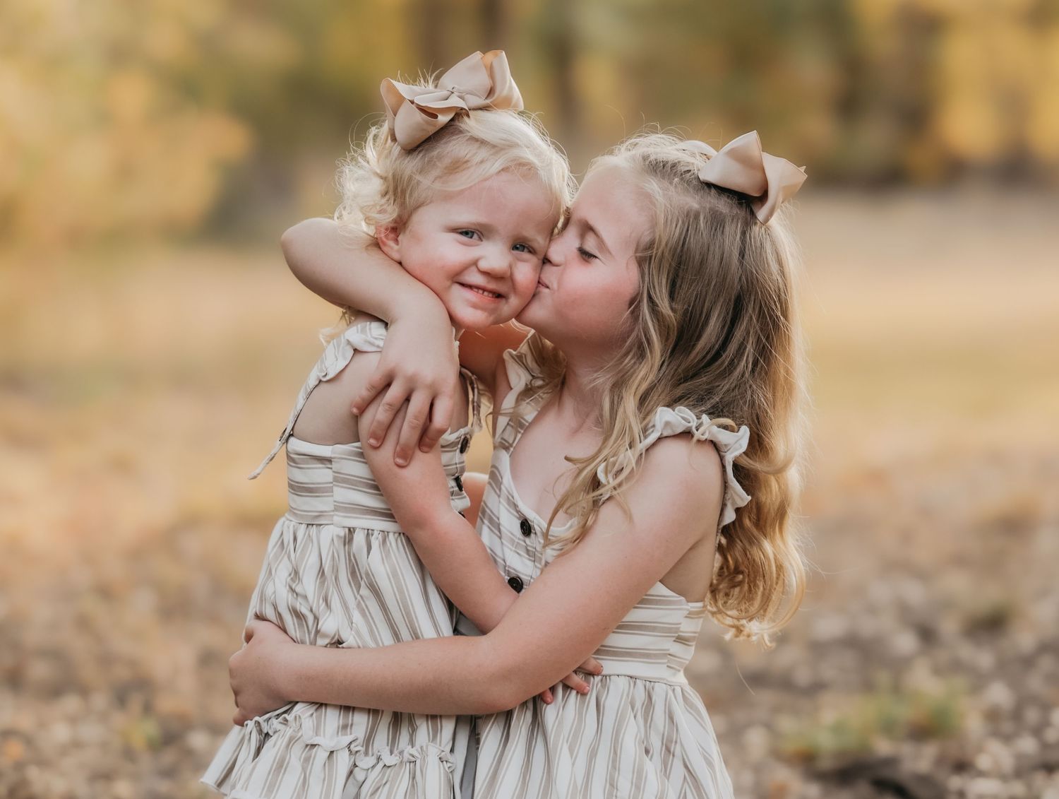 Two sisters smiling and sitting together among colorful fall leaves during a family photo session in Temple, Texas