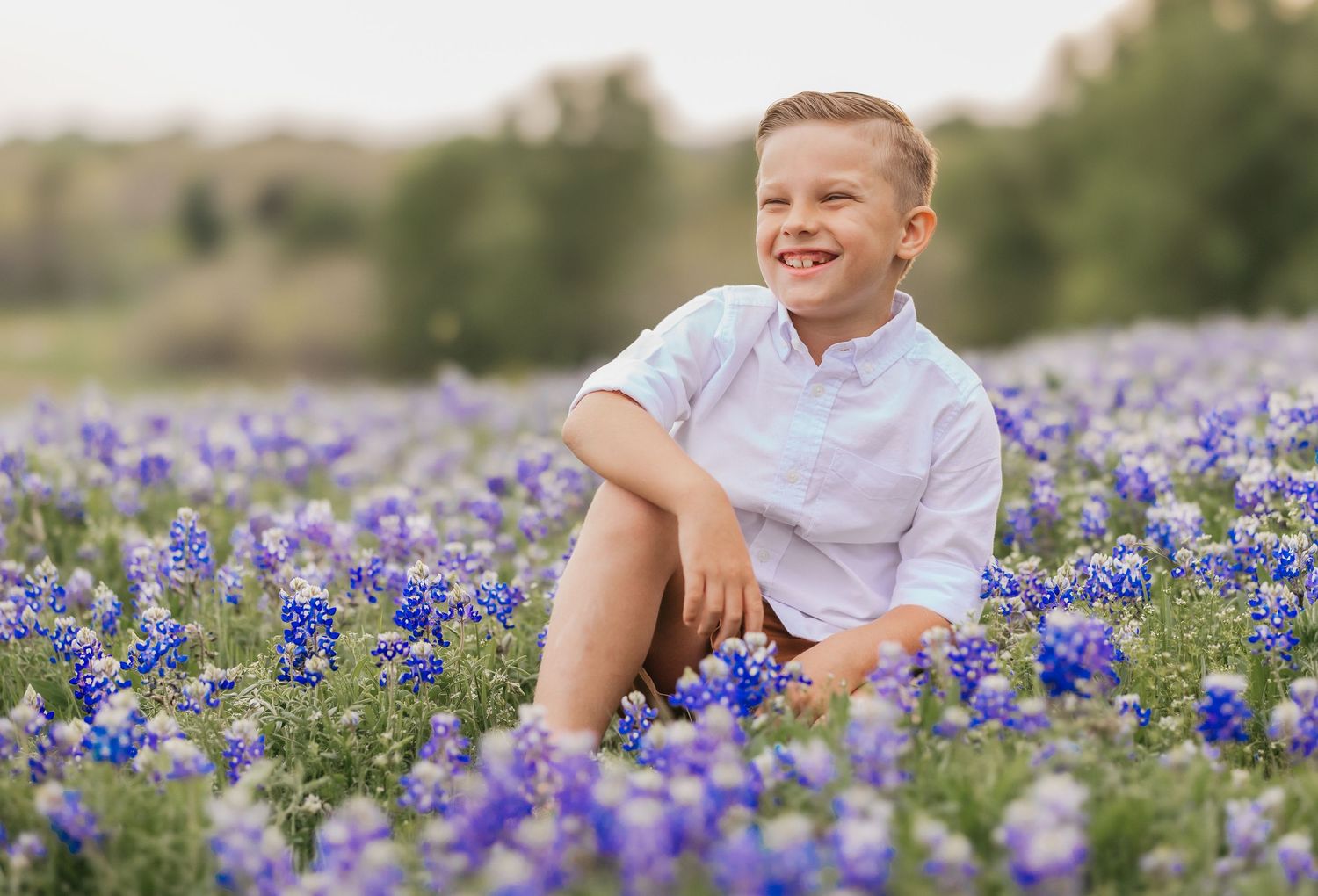Sweet boy sitting happily in a field of blooming bluebonnets in Belton, Texas during a spring photo session