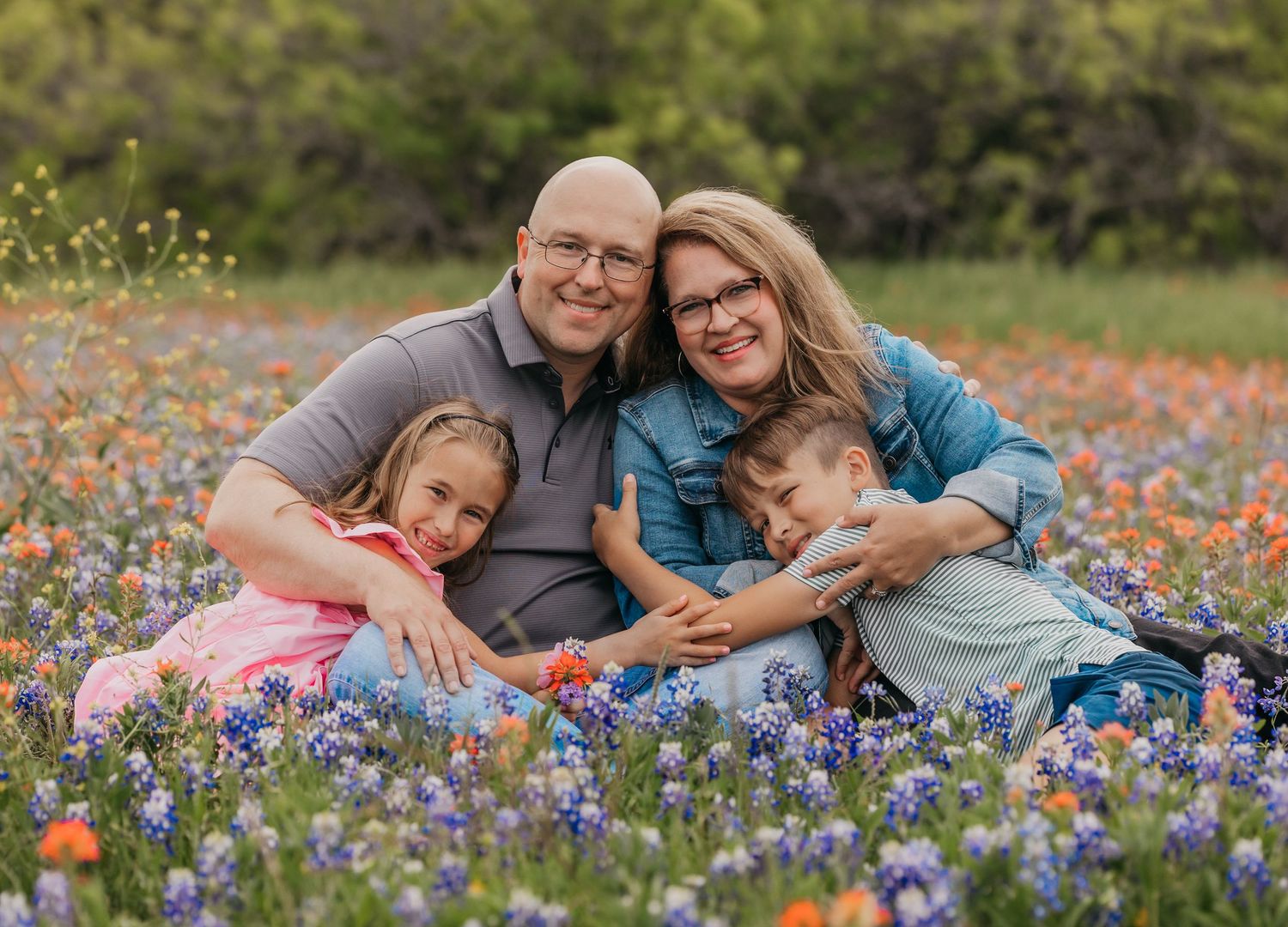 Family of four posing happily in a field of blooming bluebonnets in Temple, Texas during a spring photo session