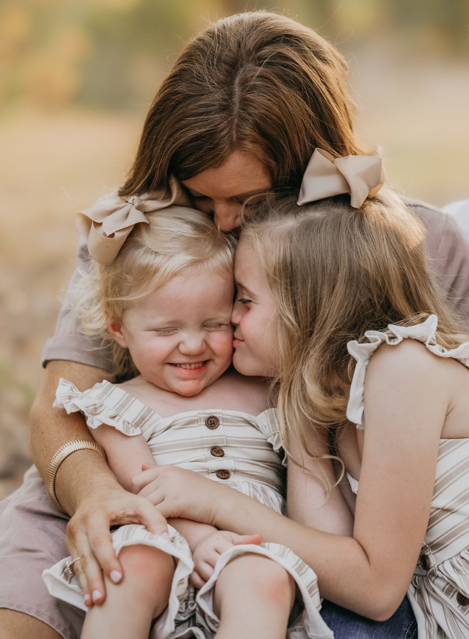 Mom kissing her two sweet daughters during a fall mini session surrounded by colorful autumn leaves