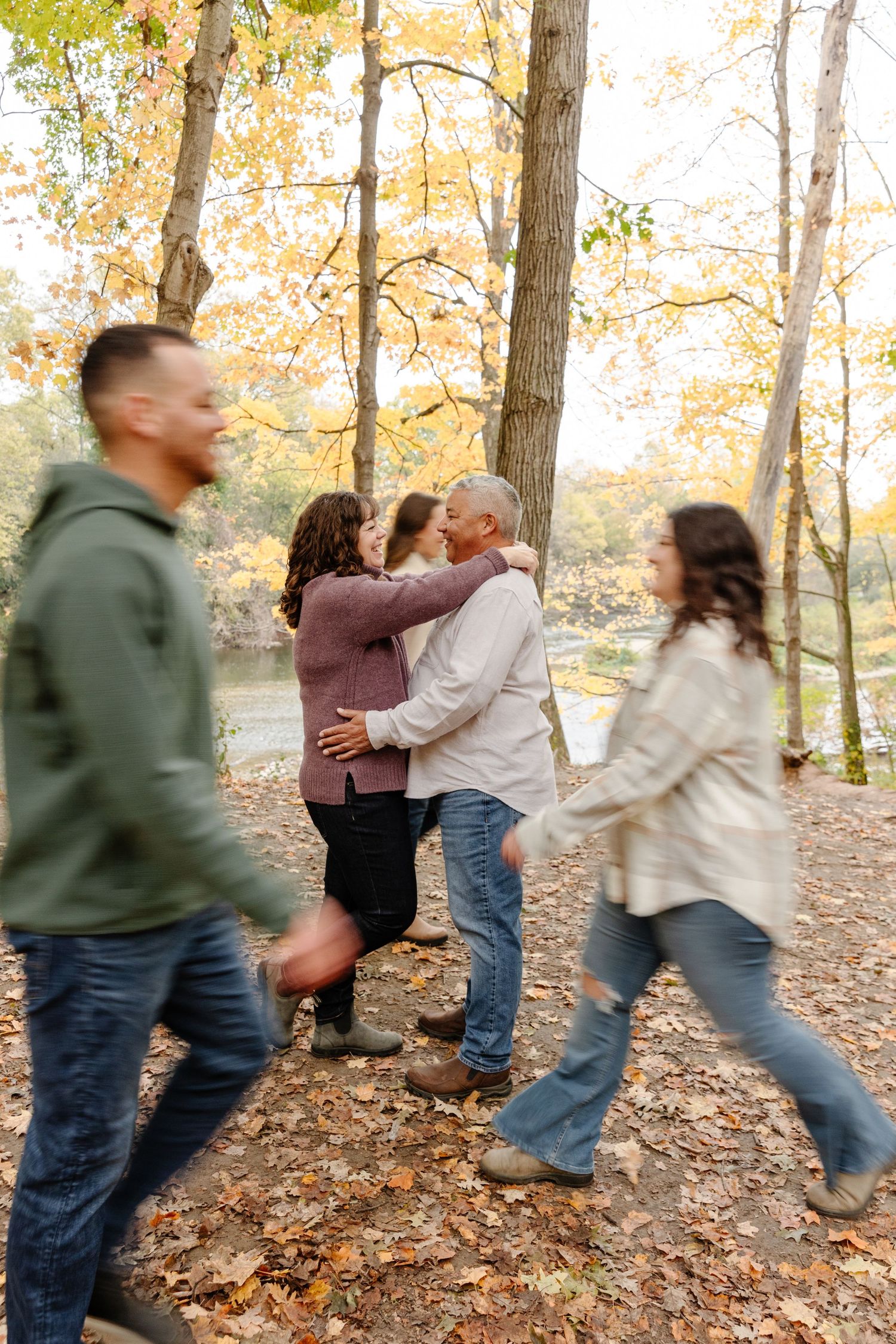 People playing and running through fallen leaves in an autumn forest setting.