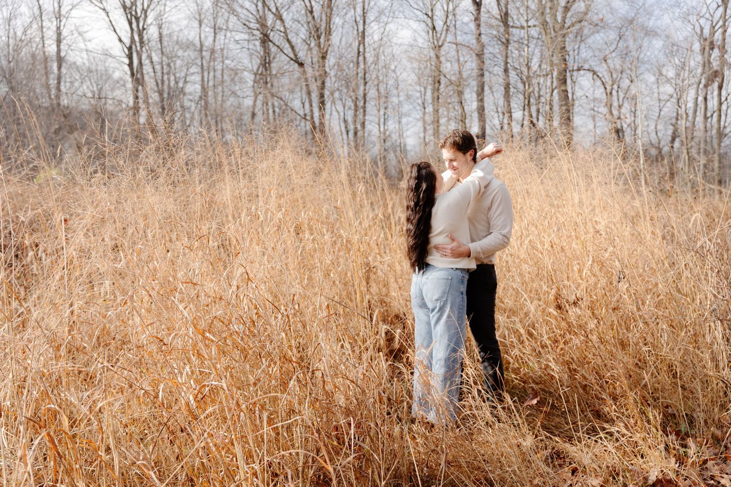 A couple embraces in a field of tall dried grass during autumn.