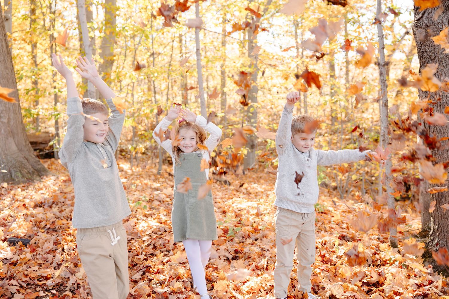 A family plays together in a forest during autumn while throwing colorful fall leaves in the air.