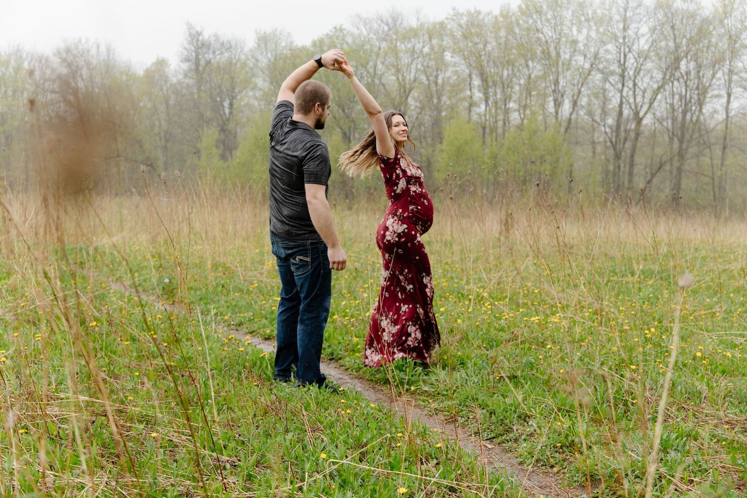 A couple dances together in a scenic meadow surrounded by tall grass and trees on a misty spring day.