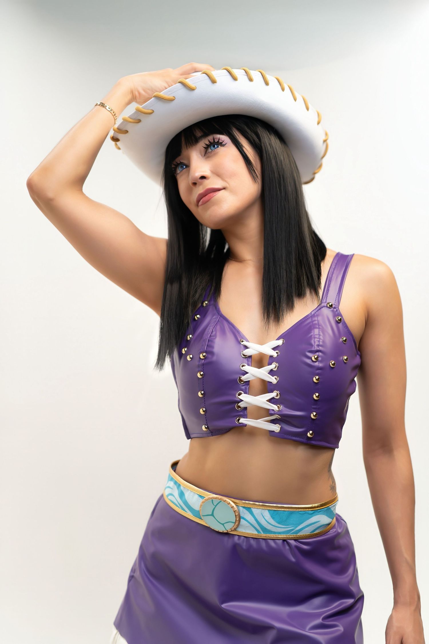 Woman in purple corset top and skirt with white cowboy hat poses confidently against light background.