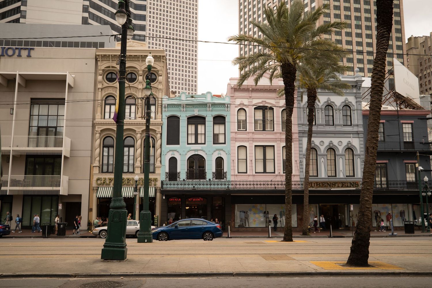 Colorful historic buildings line a New Orleans street with palm trees and a blue car parked outside.