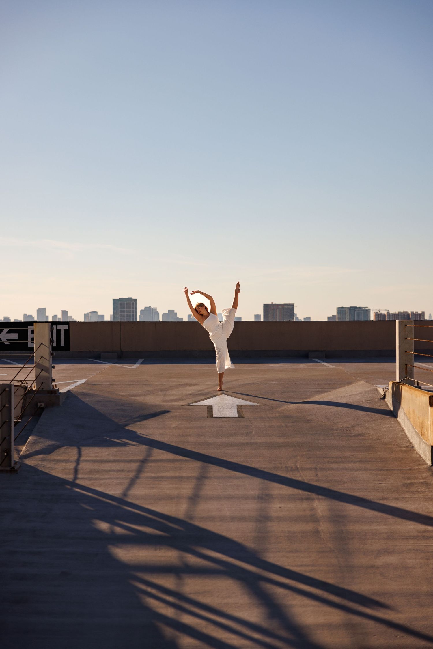 Dancer in white performing on urban rooftop against city skyline.