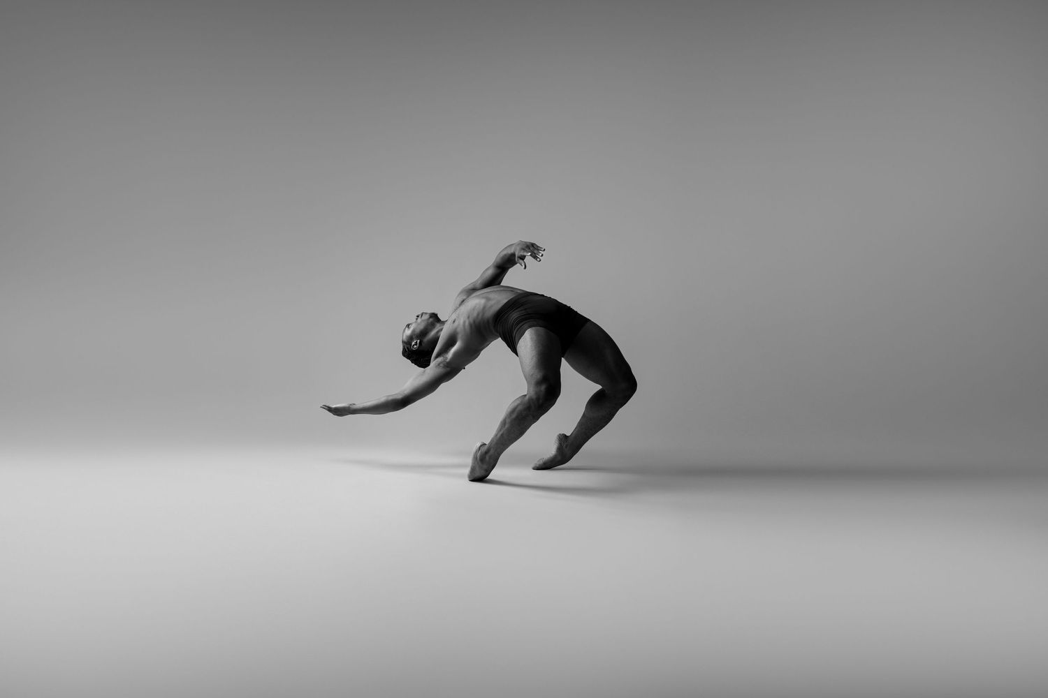 Black male dancer hinging backwards with his muscles stretching in a black and white image.