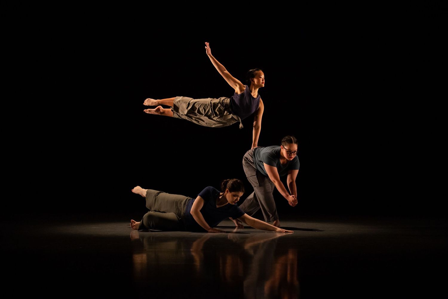 Dancers perform contemporary choreography on a dark stage creating dramatic silhouettes and formations.