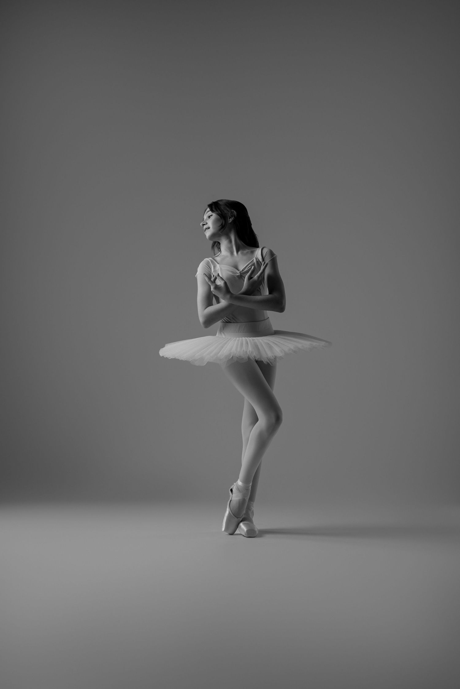 Black and white photo of an elegant ballerina in a tutu and pointe shoes striking a graceful pose in a studio.