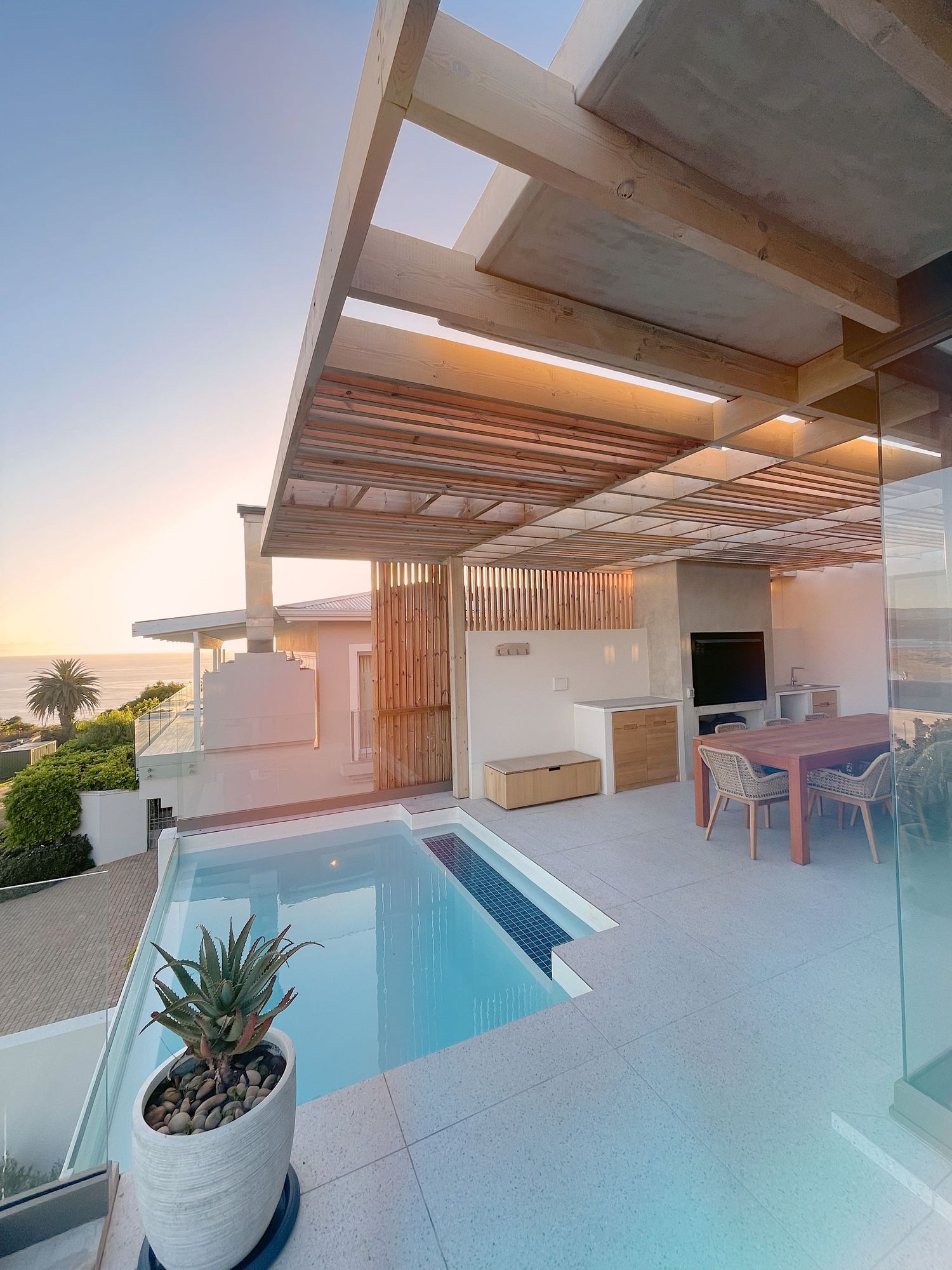Luxury rooftop terrace with small pool, wooden pergola, dining area, and ocean sunset views.