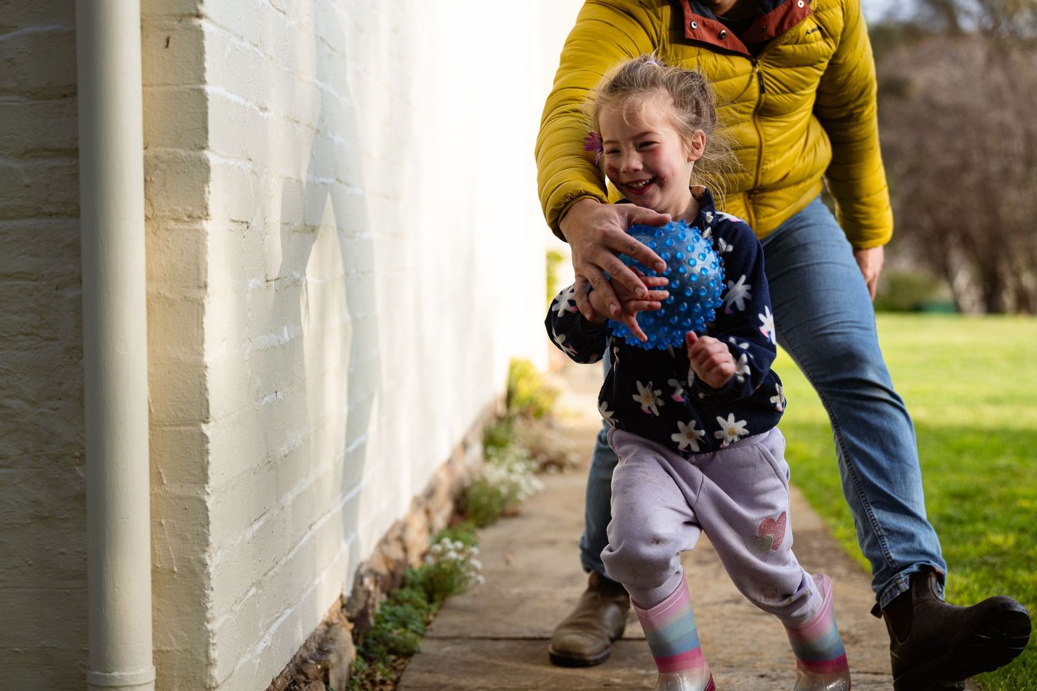 Two people playing with a small child on a sunny day outside a white-columned building.