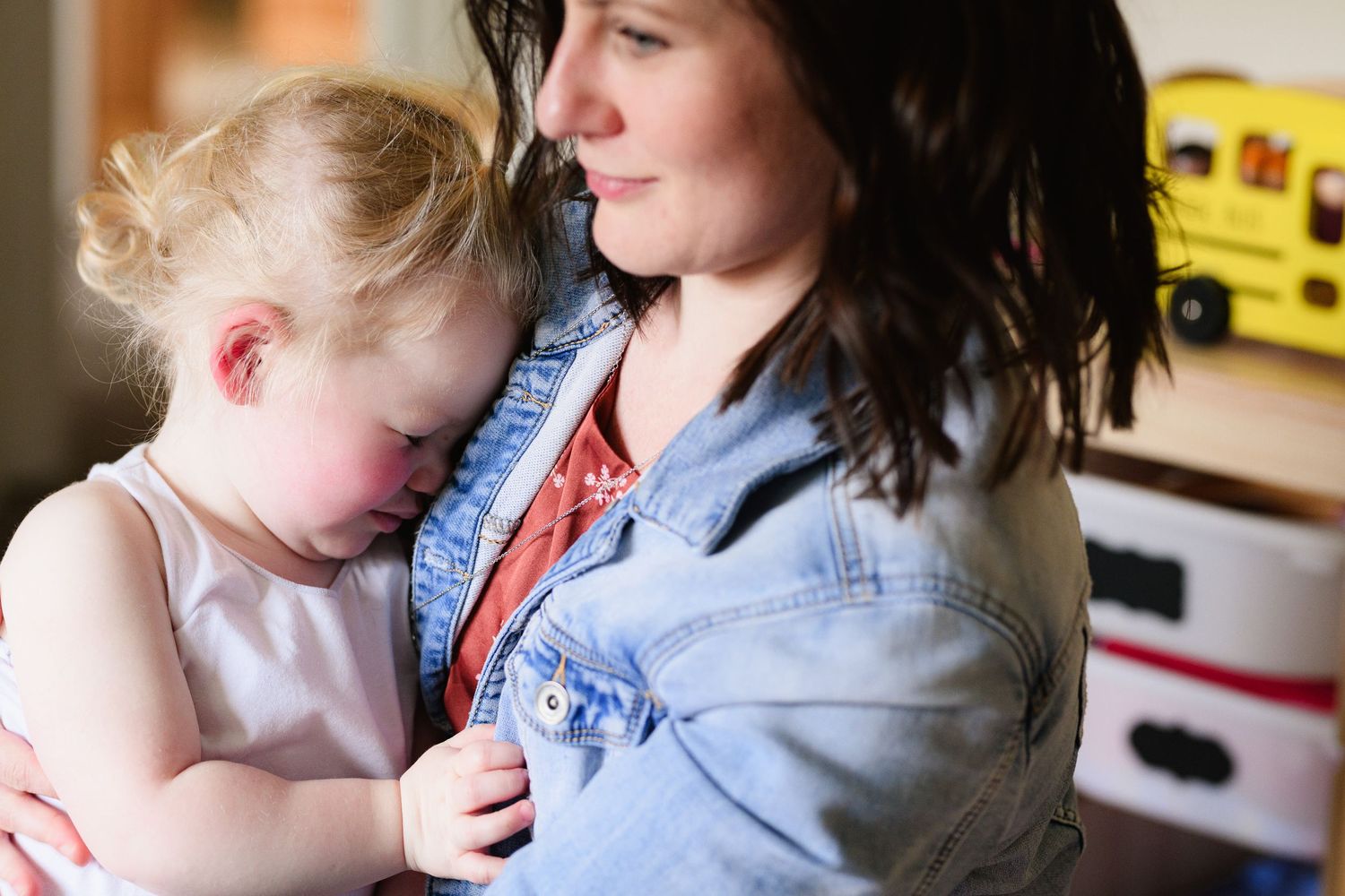 A parent and young child share a tender moment while reading a book together on a couch.