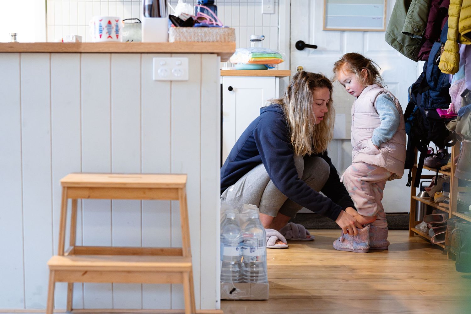 Adult and child interact while sitting on a wooden floor in a bright home interior with wooden furniture.