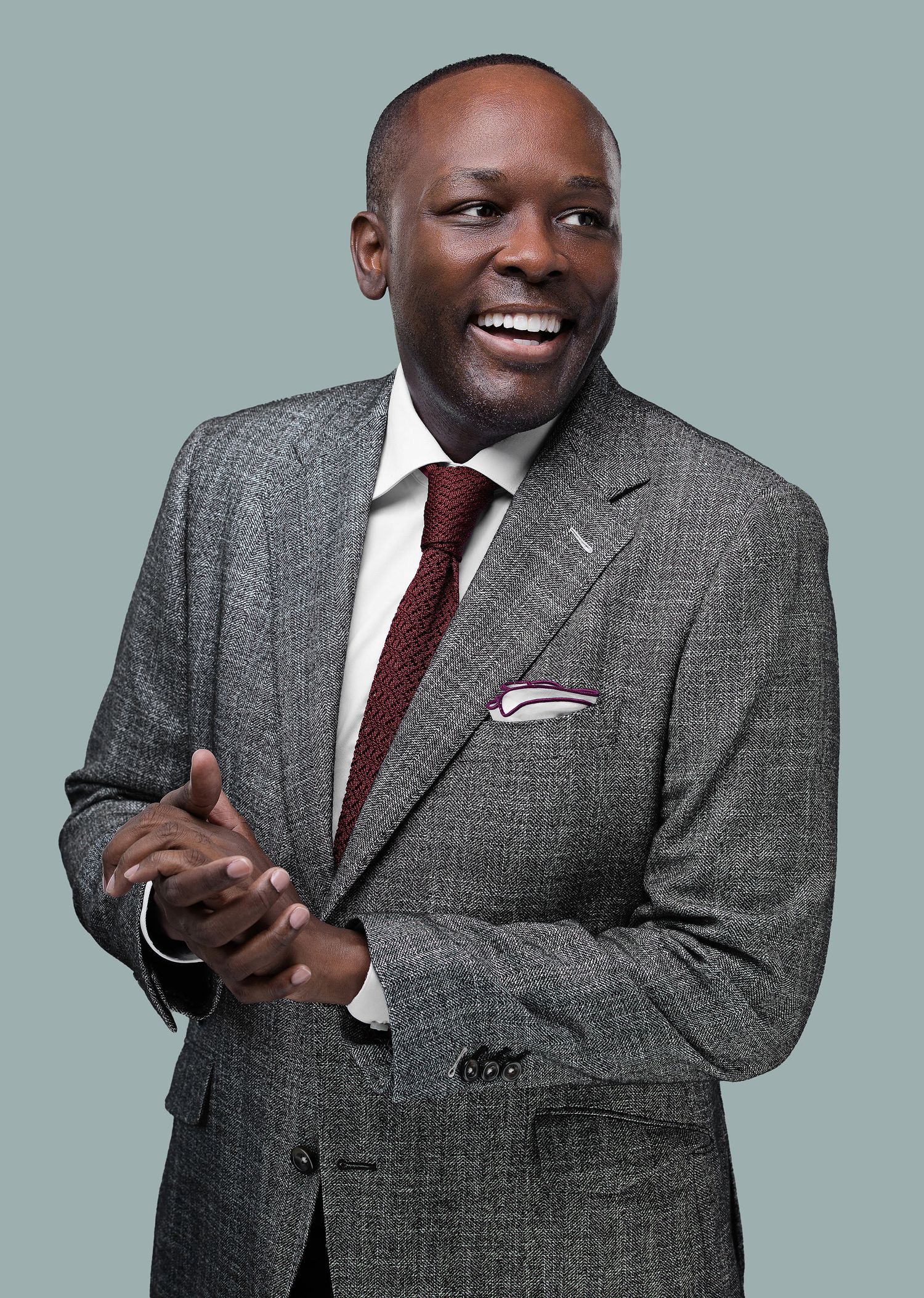 Professional portrait of a person in a grey suit and burgundy tie smiling warmly against a light blue background.