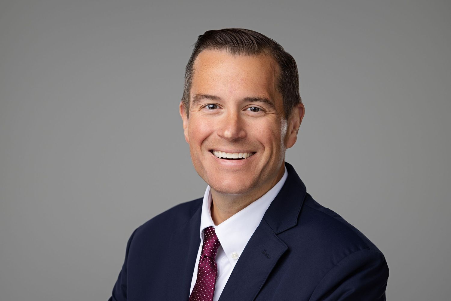Professional business headshots of people in suits and ties against a neutral gray background.