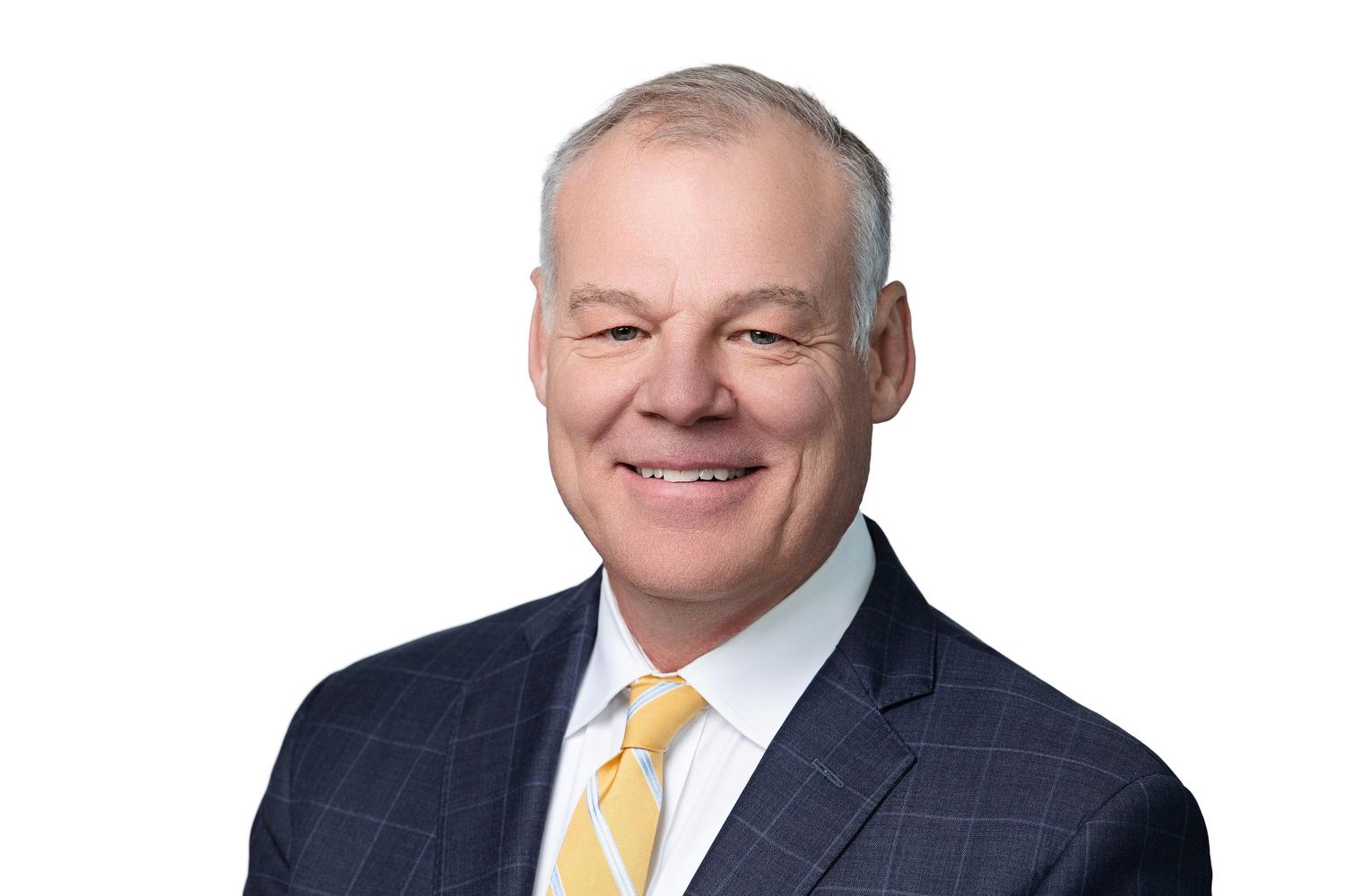 A person wearing a dark suit and yellow tie smiles while standing against a light background.