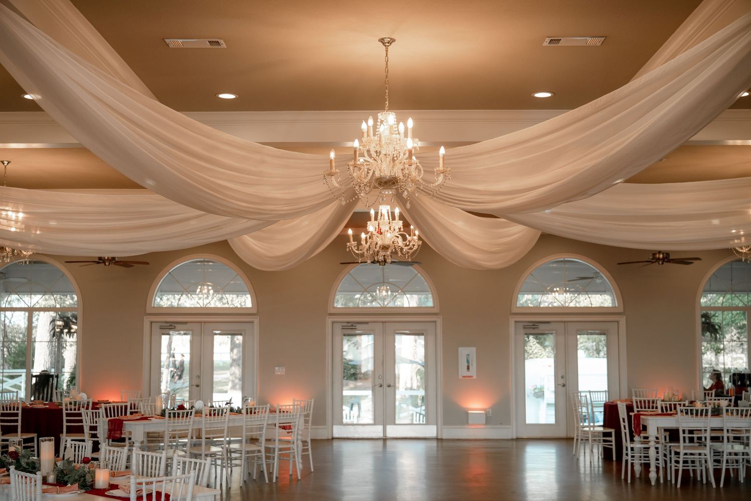 Ballroom at Willow Creek Wedding Venue in  DFW venue featuring chandeliers and heavy white draping and large windows