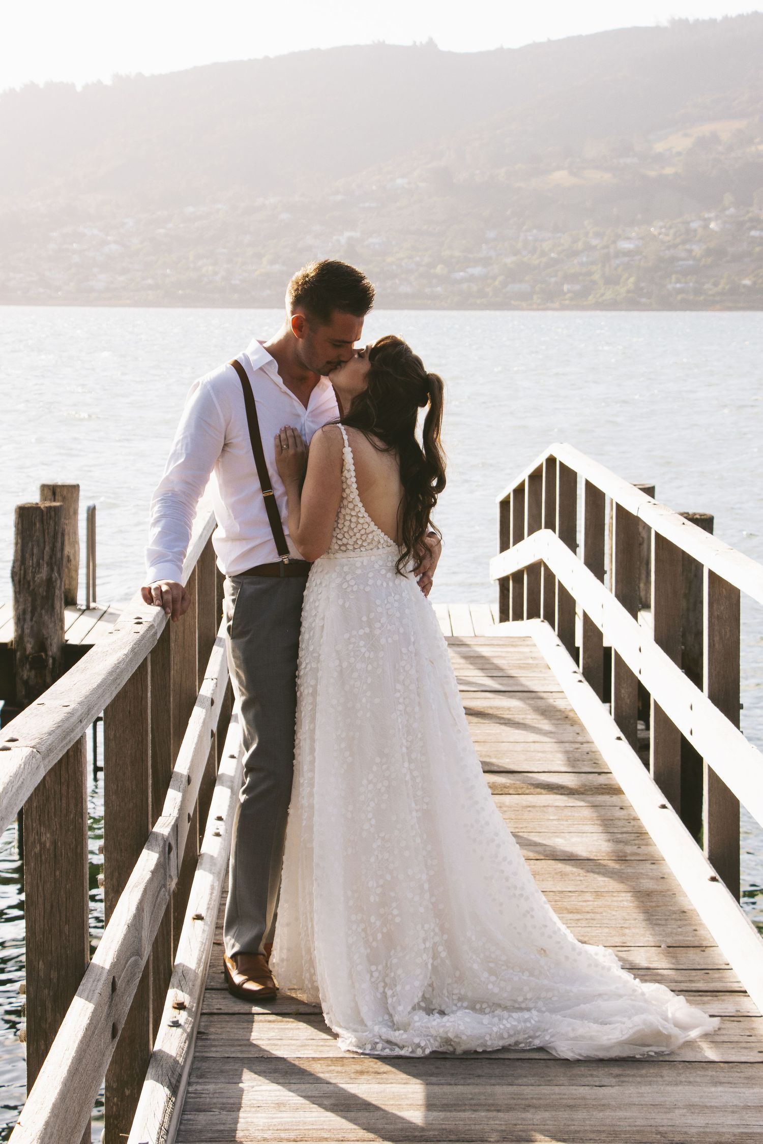 A romantic moment between newlyweds on a wooden pier overlooking calm waters.