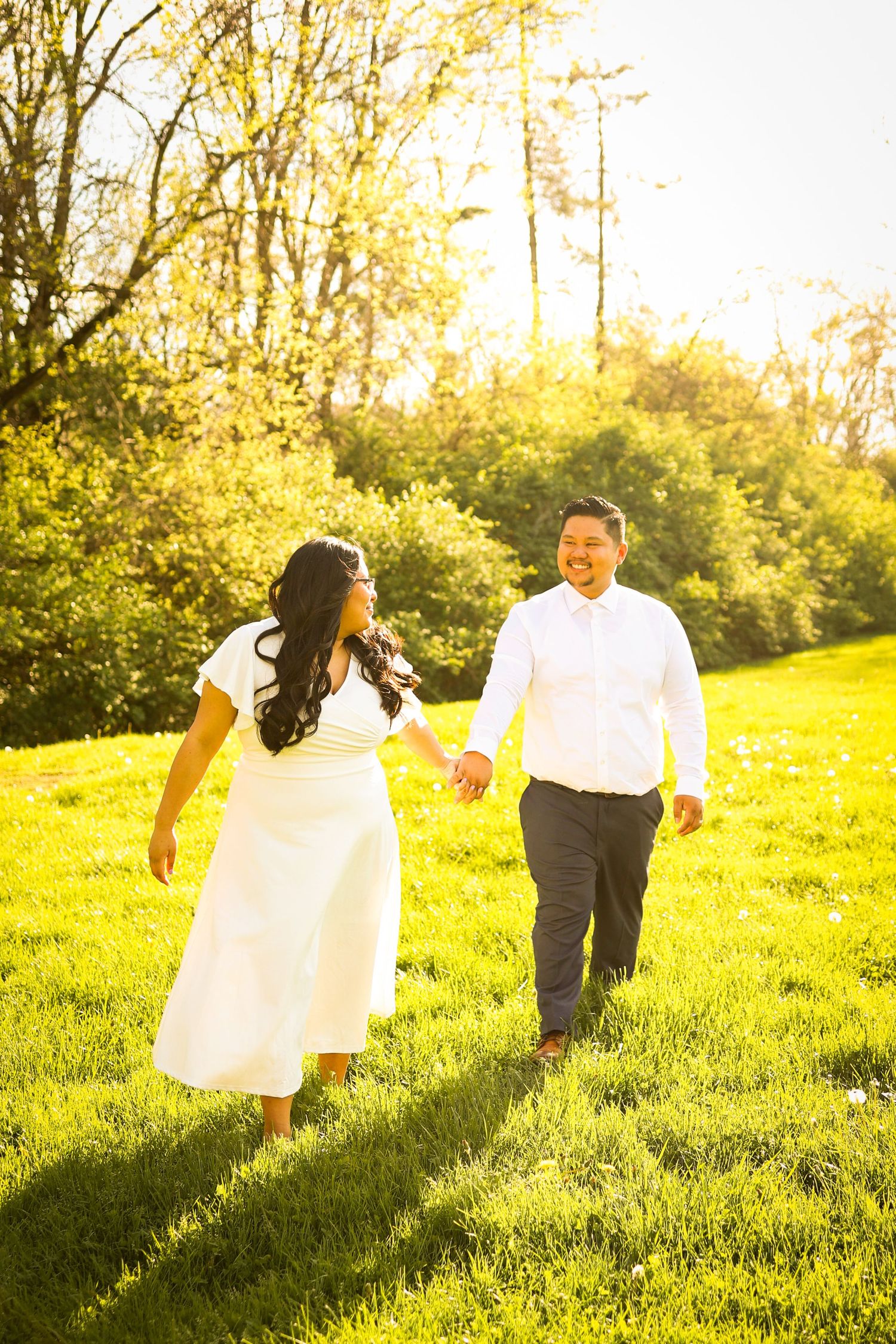 A couple walks hand in hand through a sunlit meadow on a warm golden afternoon.