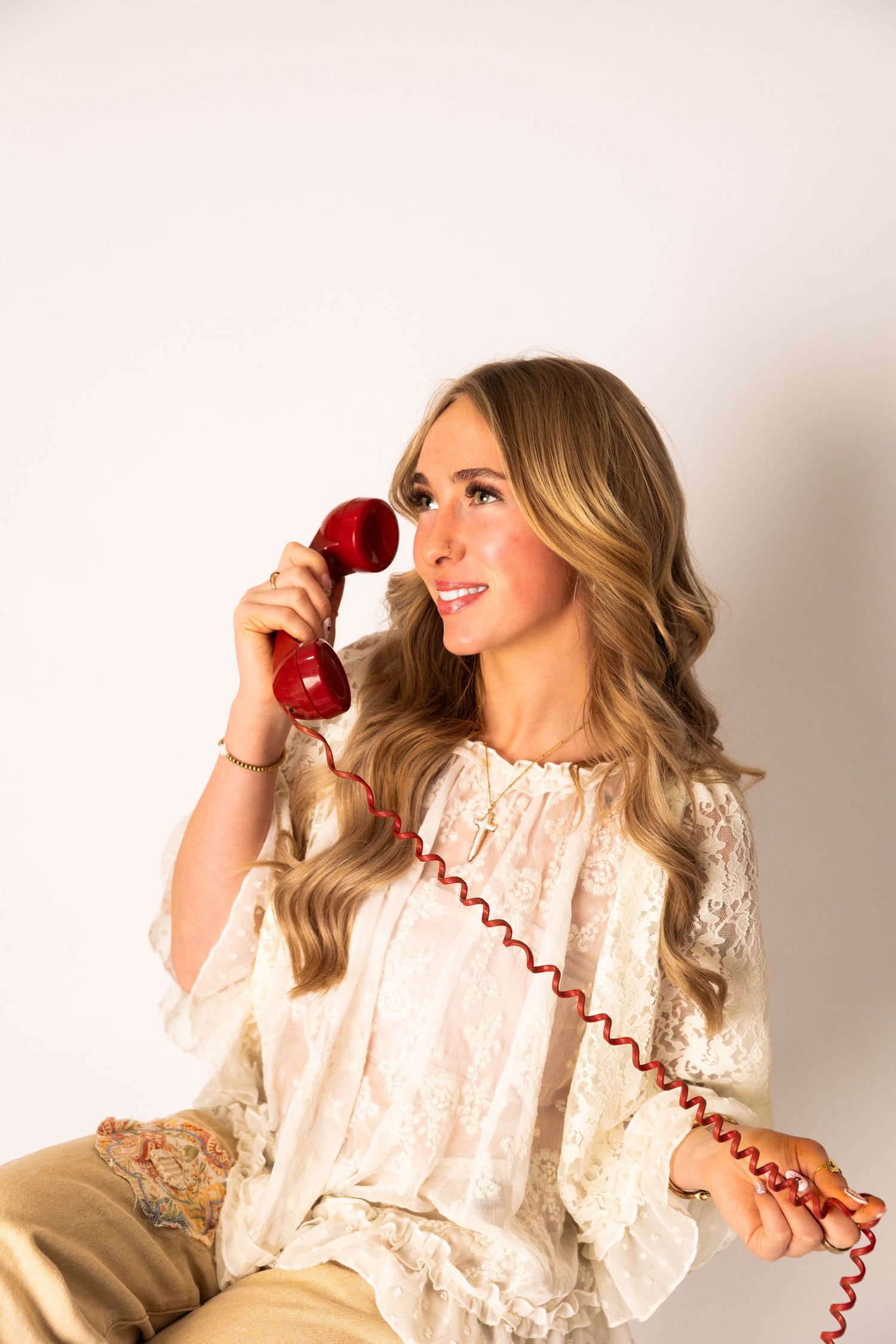 A person in a vintage white lace dress poses playfully with a red retro telephone cord in a series of lifestyle shots.