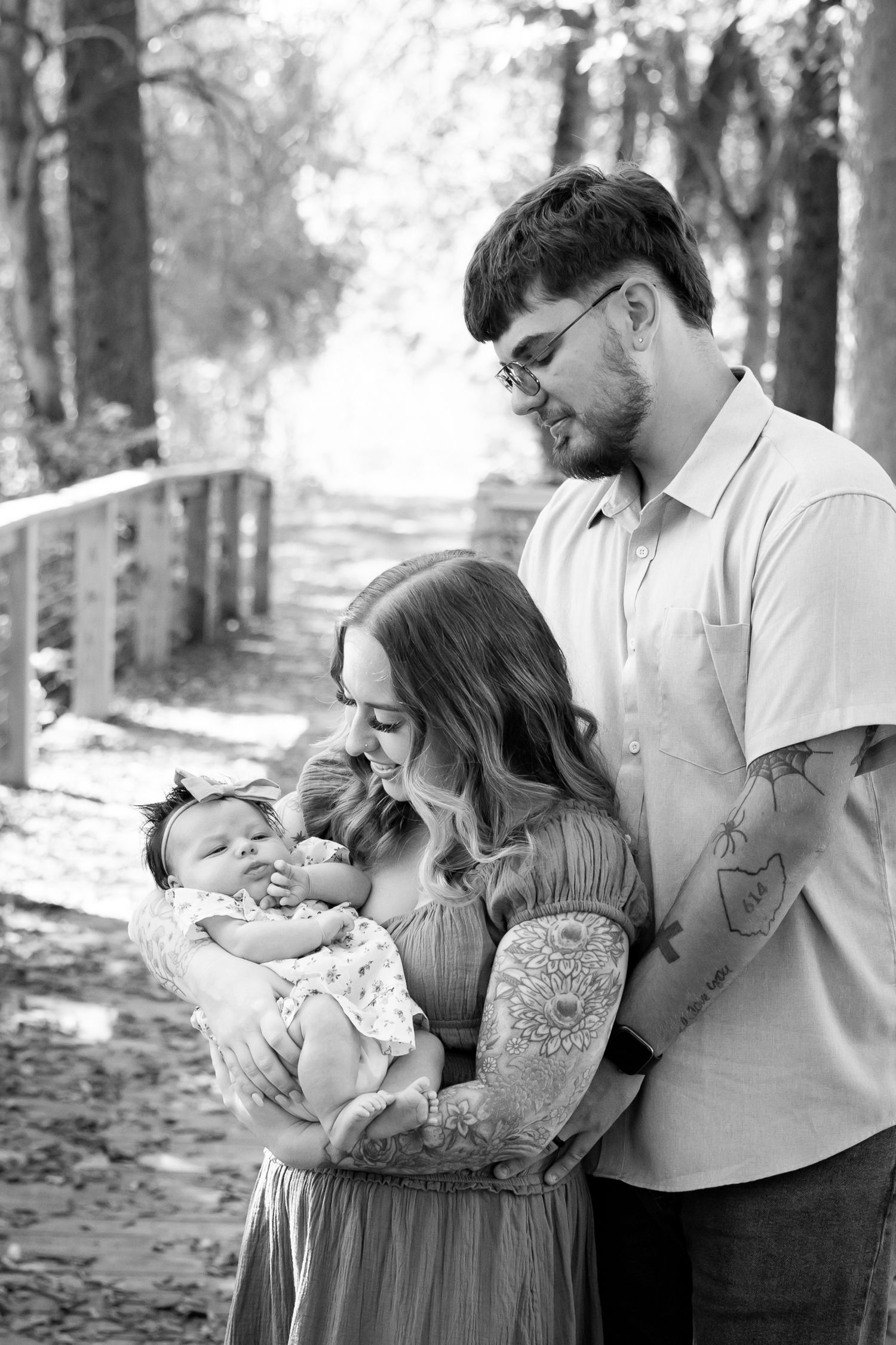 A couple in a wooded setting share tender moments with their baby in a series of black and white photographs.