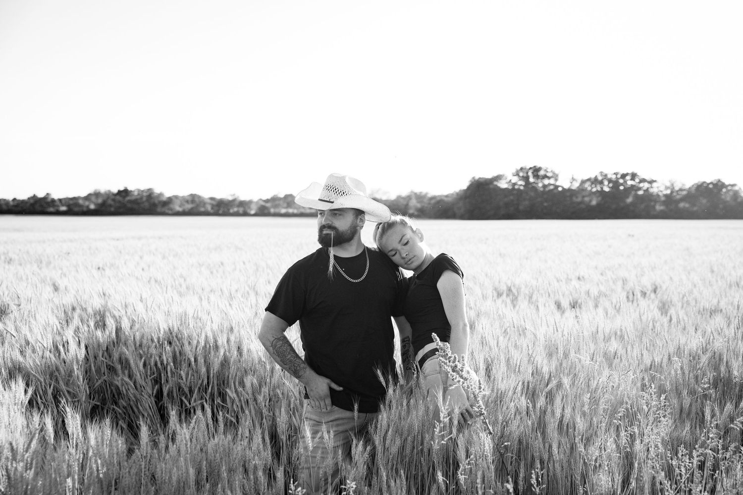 A couple embraces romantically in a golden wheat field at sunset creating a silhouette against the sky.