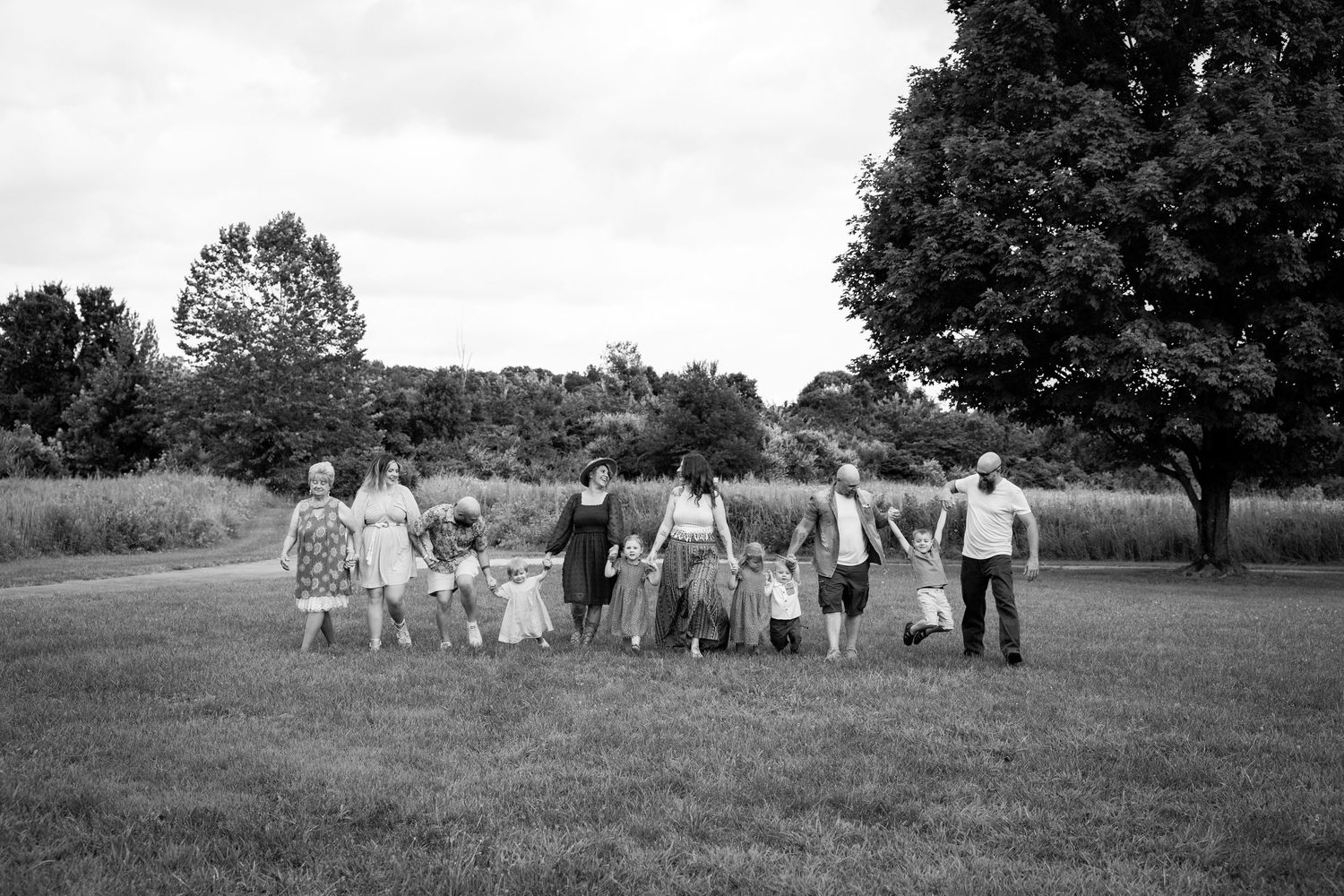 A black and white panoramic photograph shows a group of people gathered outdoors in a rural setting with trees in the background.