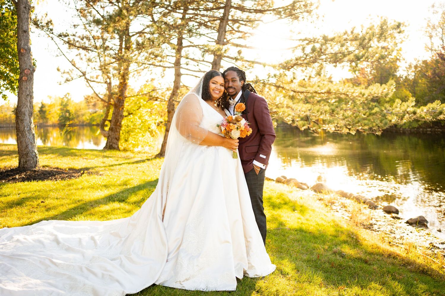 Newlywed couple embracing by a sunlit lake on their wedding day with pine trees and golden light in the background.