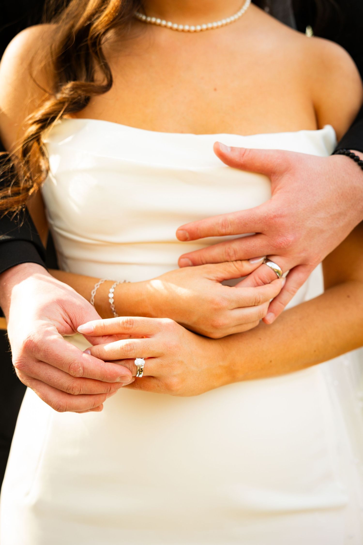 Close-up of hands adjusting a white wedding dress bodice with a pearl necklace visible in the frame.