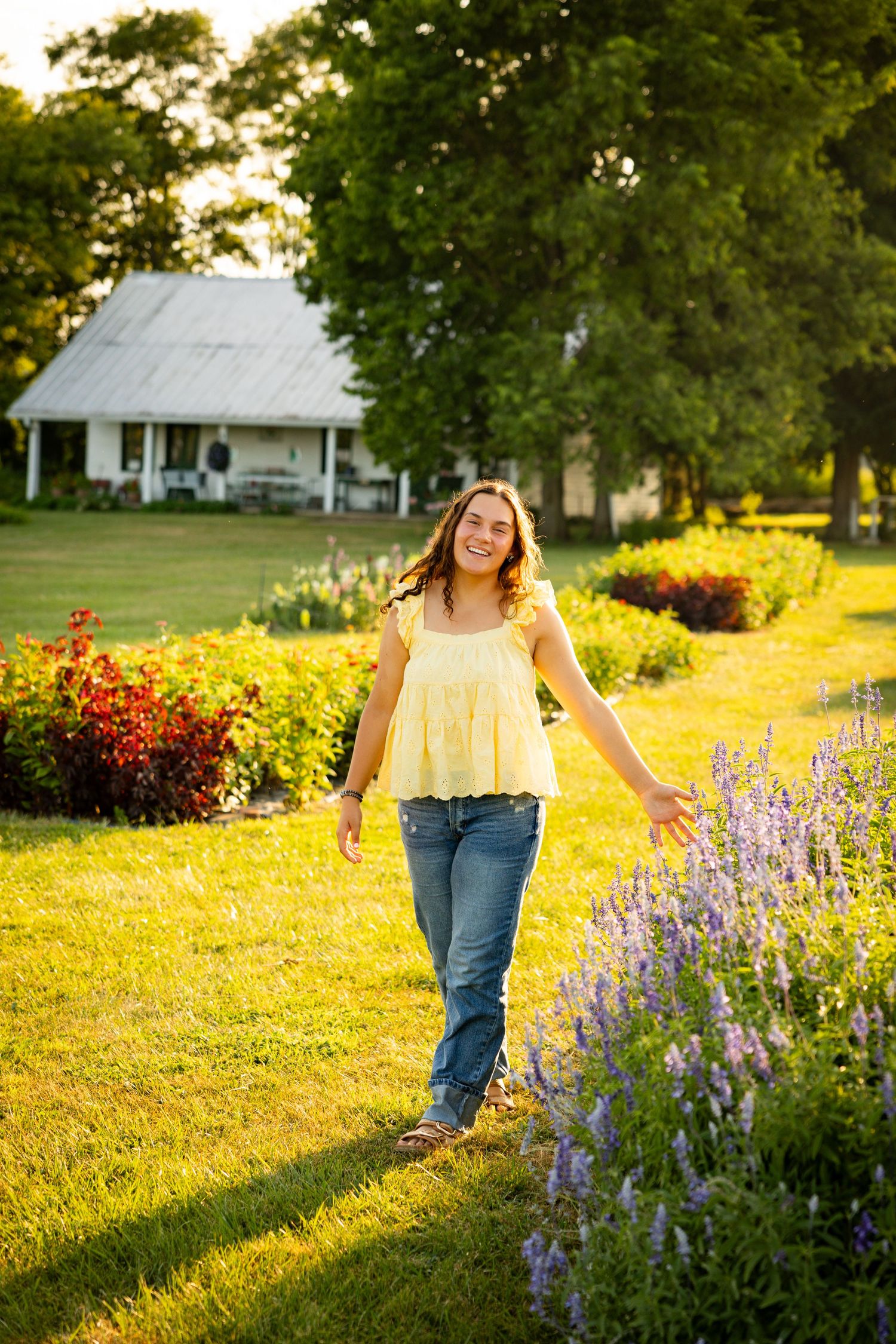 A person walks through a vibrant garden path with purple wildflowers and golden sunlight during sunset.