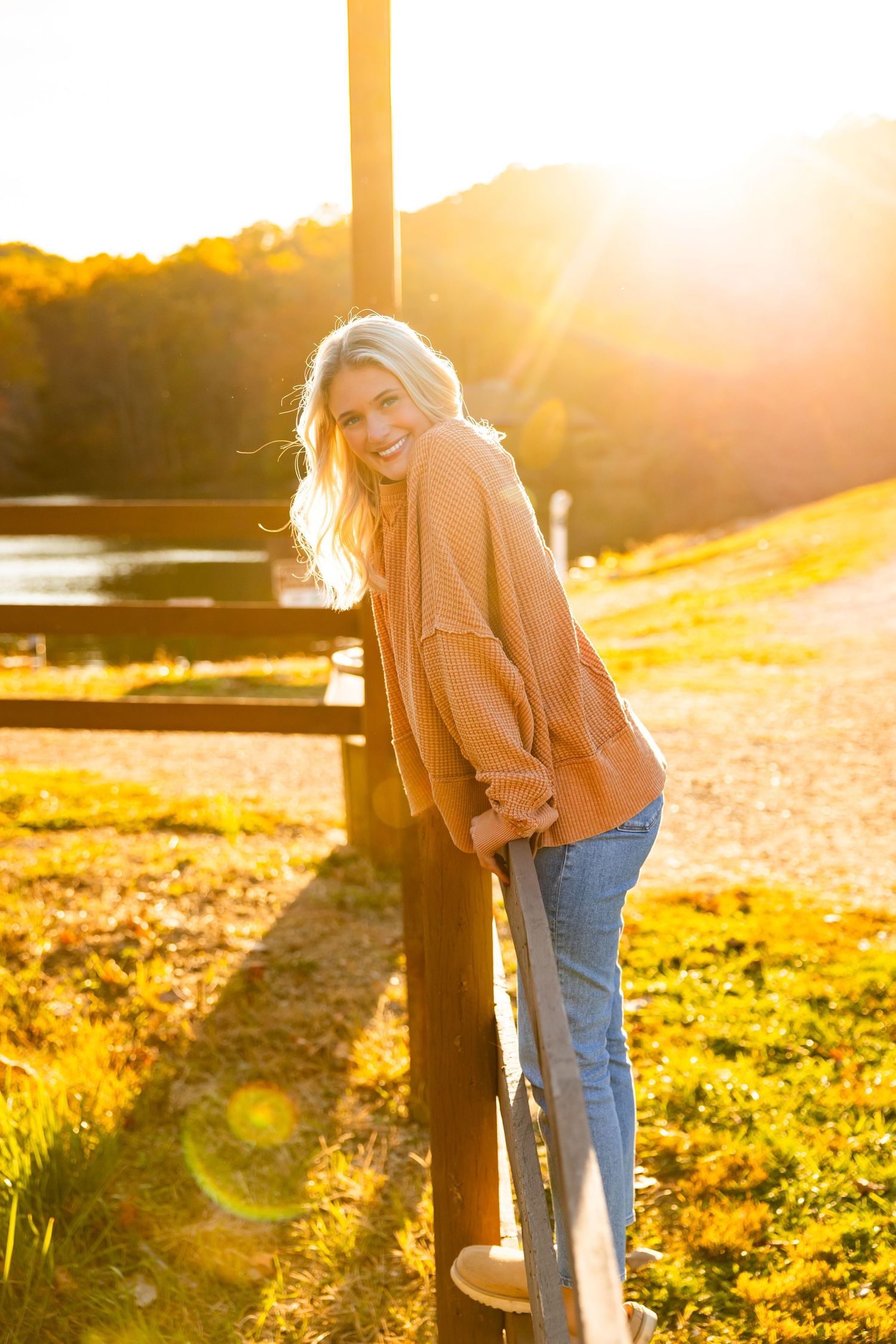 A figure leans against a pole in a sunlit field during golden hour as lens flares create a dreamy atmosphere.